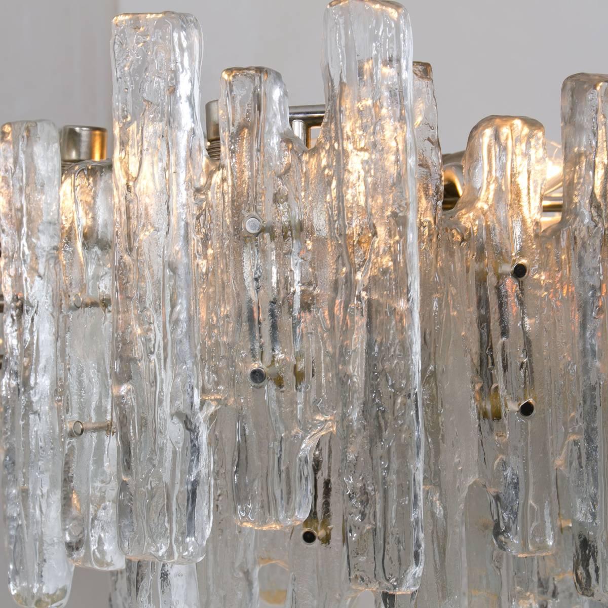 A high end elegant modern chandelier, manufactured by Kalmar Austria in the 1960s. Lovely design, the chandelier has 18 sockets 40W and three layers of extremely stylish textured solid ice glass sheets dangling on it. 
Illuminates