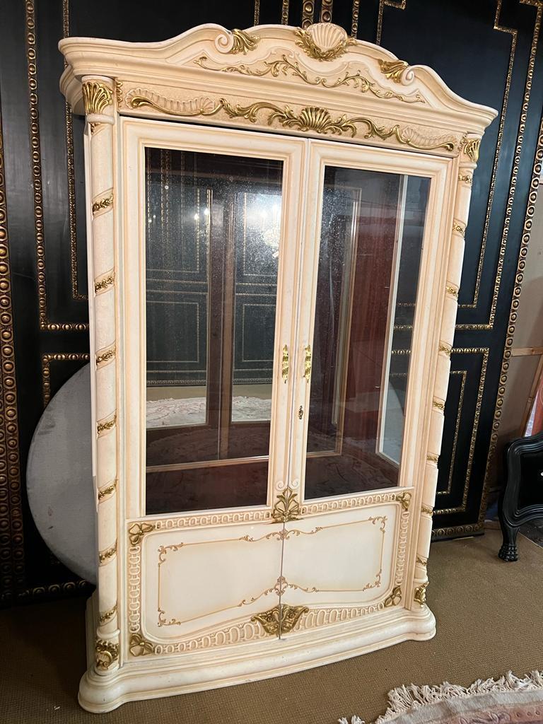 Massiccio, finemente intagliato in legno di faggio, colorato e dorato. Corpo bombato alto-rettangolare, semitondo e a una porta, smaltato su tre lati. L'intera vetrina può essere smontata. Su piedi curvi cornice smerlata a un'anta. Parete posteriore