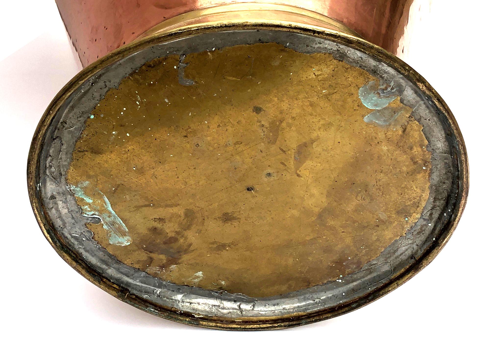 of extra large scale and composed of contrasting metals; with wide protruding mouth connected to the ovoid copper body by a brass riveted ring all joined by a large brass ear or handle.