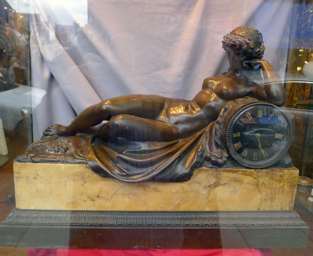 Französische Kaminsimsuhr aus patinierter Bronze und Siena-Marmor von gewaltigen Ausmaßen. Das Motiv zeigt eine nackte Jungfrau, die auf einem Löwenfell liegt und sich an die Uhr lehnt. Bei dem Motiv handelt es sich mit Sicherheit um eine
