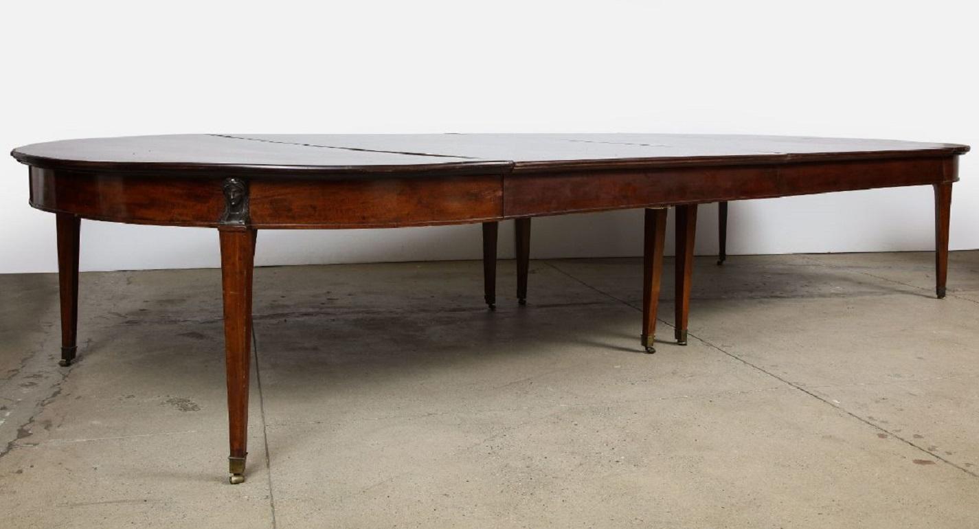 Massive French late 18th/early 19th century mahogany dining table, the solid and well-figured mahogany top with molded edge, (with later leaves which can extend the table to 262 inches!) over banded apron, the legs capped with patinated bronze term