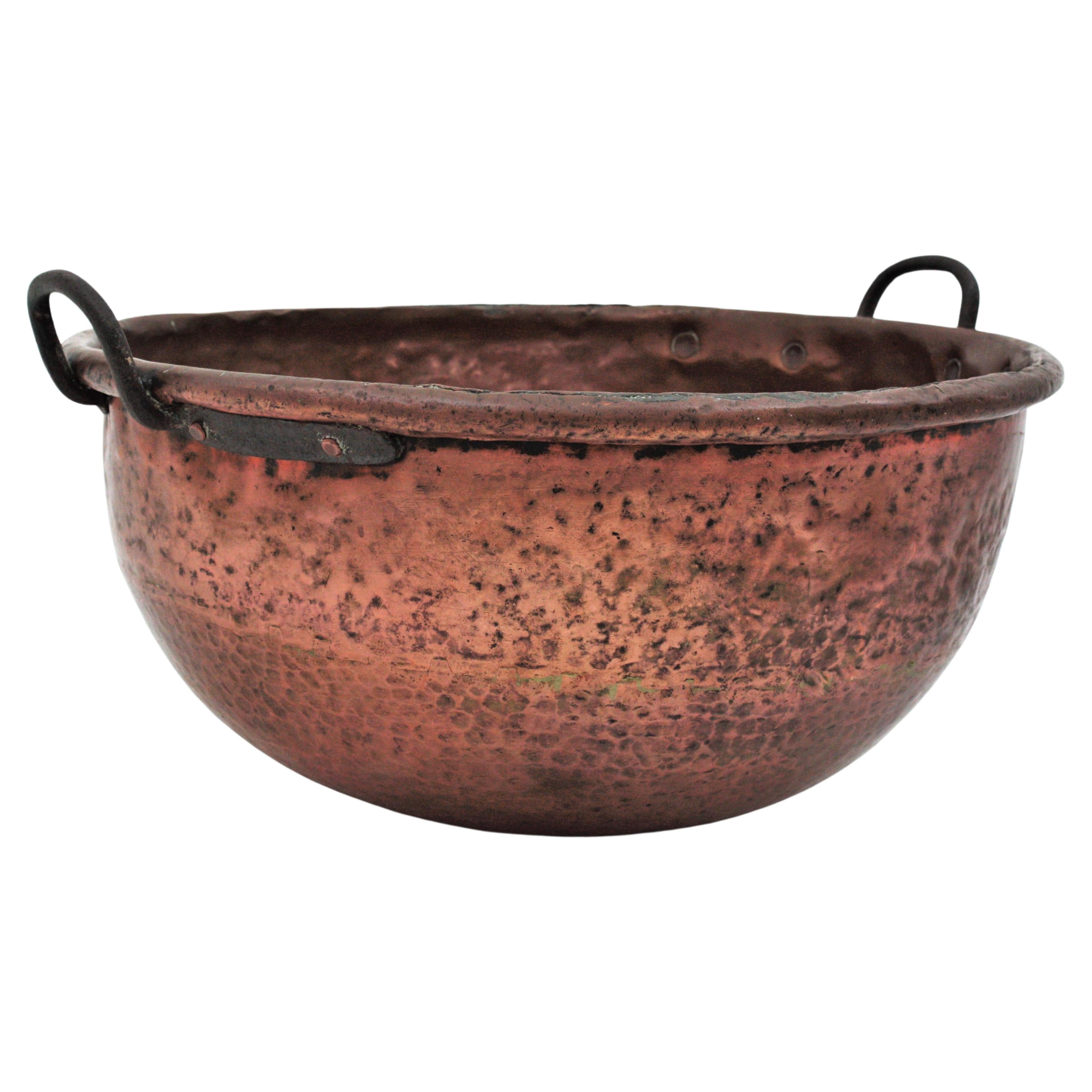 Oversized hand-hammered copper cauldron with iron handles. France, early 20th century.
This handcrafted copper cauldron has a terrific aged patina. It has a thick rolled rim and forged iron handles attached to the pot with iron studs. The copper is