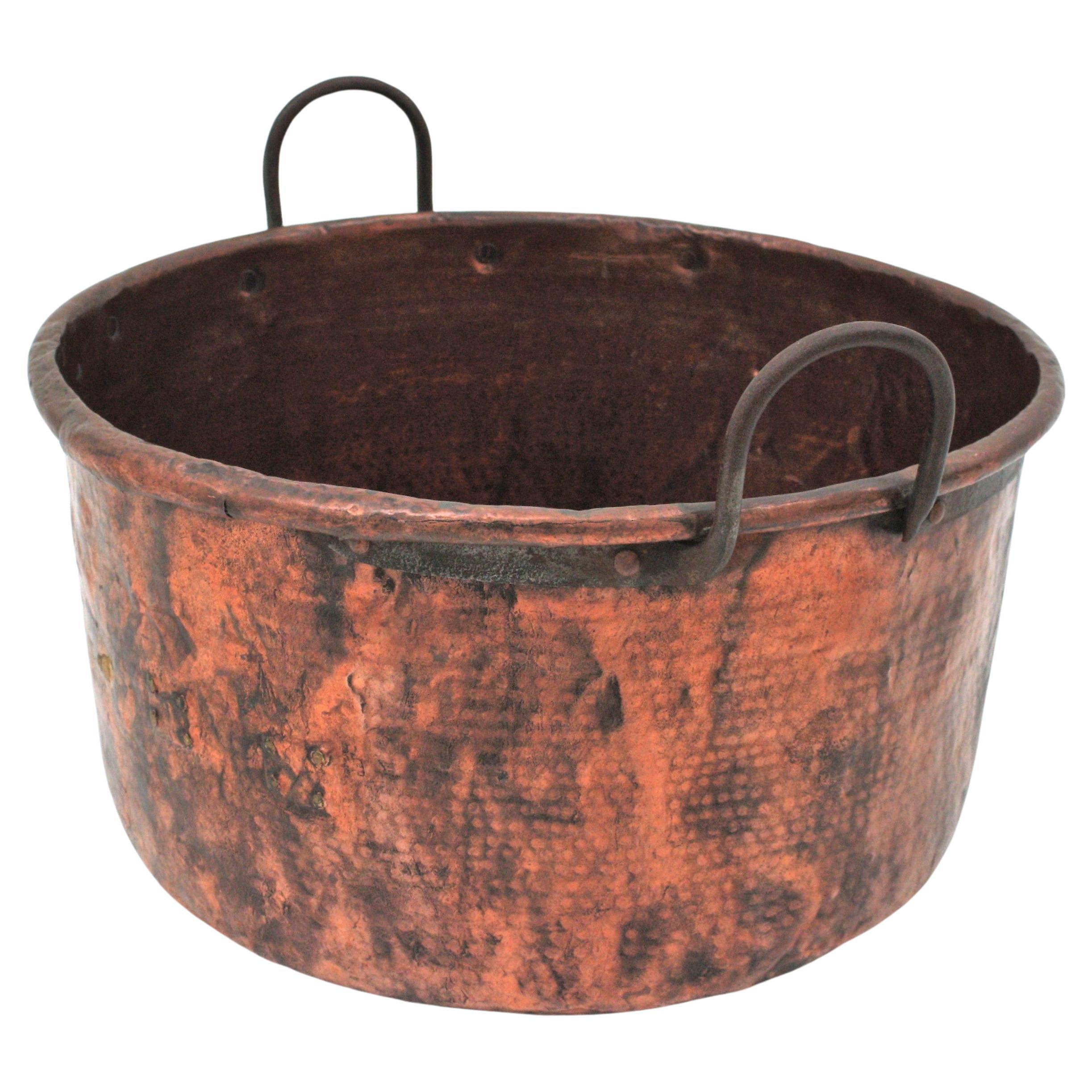 Oversized hand-hammered copper cauldron with iron handles. France, early 20th century.
This handcrafted copper cauldron has a terrific aged patina. The copper is heavily adorned by the hammer marks. 
The iron handles are attached to the cauldron