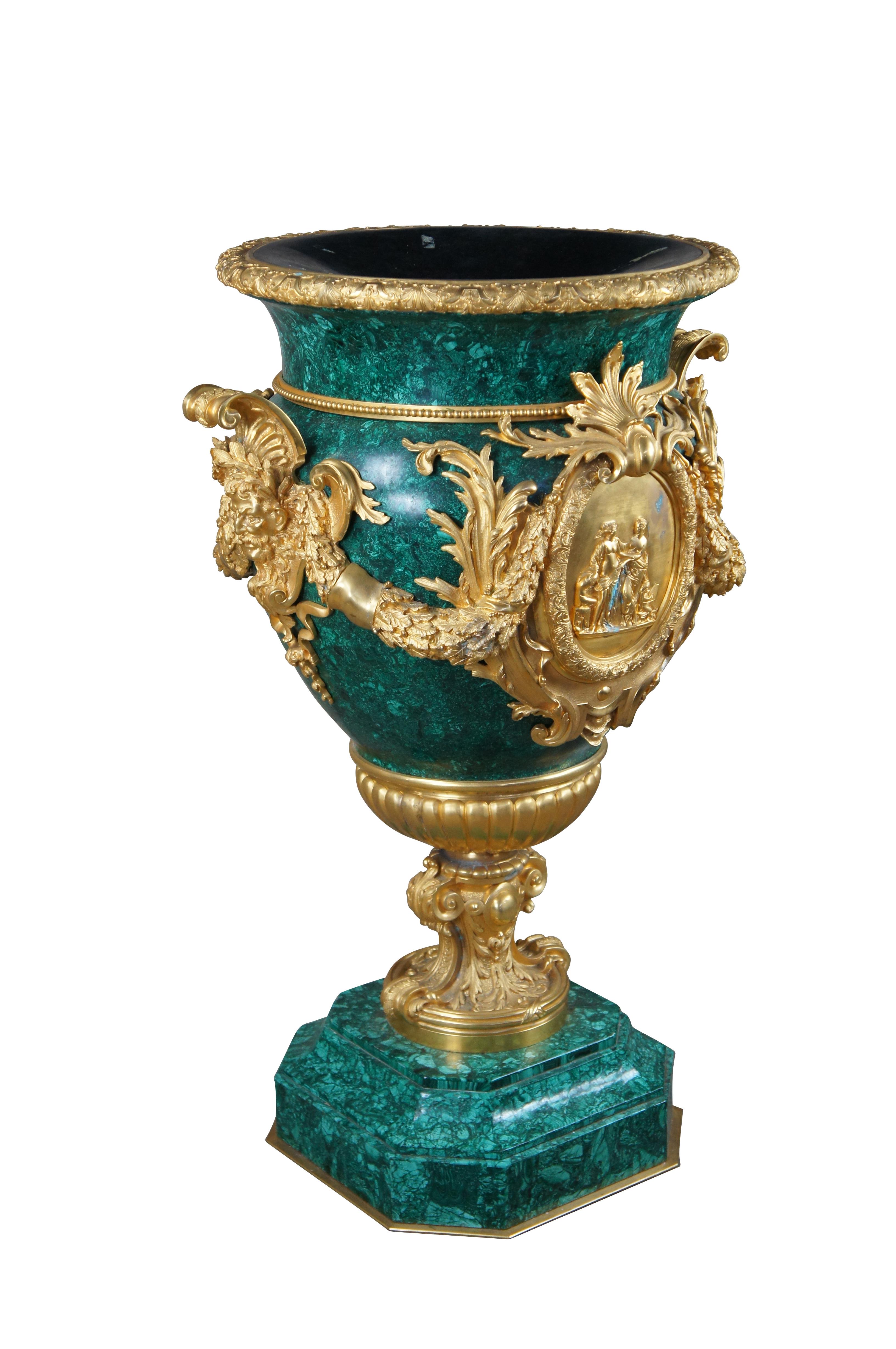 An opulent French Empire Style bronze ormolu mounted malachite urn or jardiniere. Features a rim cast with shells, foliage and bellflowers, the body centered on each side by a medallion depicting classical maidens and flanked by figural Bacchus mask