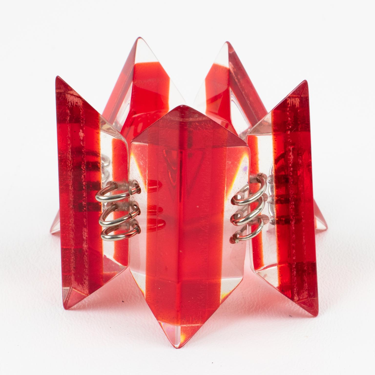 Dieses attraktive Gliederarmband aus massivem Lucite hat die Form eines geometrischen Eiswürfels in laminierter transparenter und leuchtend roter Farbe mit versilberten Metallbeschlägen. Es gibt keine sichtbare Herstellermarke.
Das Armband ist in