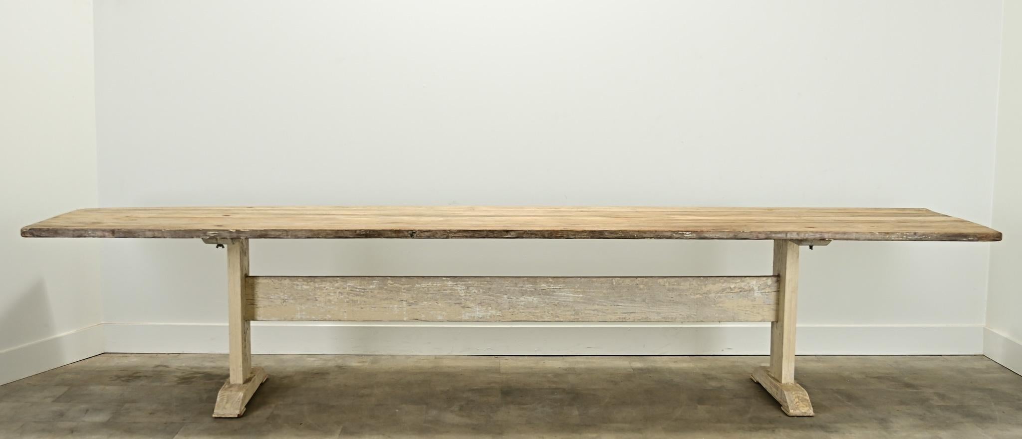 This massive Swedish Gustavian pine dining table is over 12 feet long, (12’-3 ⅝” to be exact). The simple wooden top sits over a pair of hand-cut and painted trestle base legs, each resting on a plinth base and connected by a cross stretcher. The