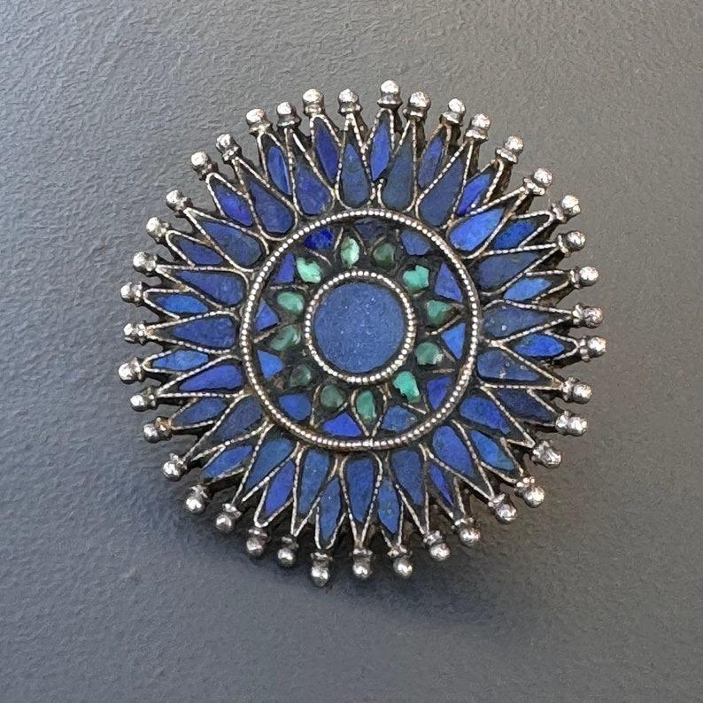 This exquisite cocktail ring showcases intricate craftsmanship and a rich ethnic/tribal aesthetic. The piece features a floral design with inlaid lapis and turquoise stones, highlighting the skilled artistry of early to mid-20th century jewelry.