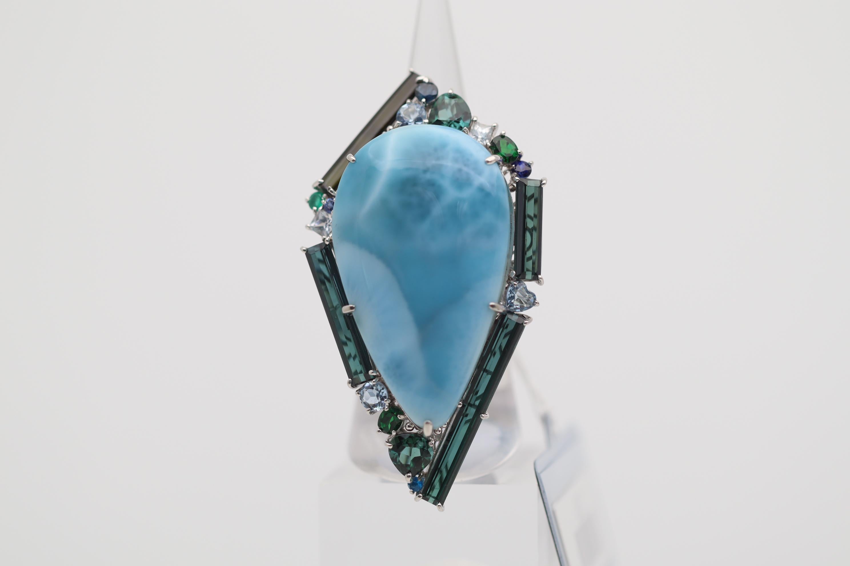 A massively impressive cocktail ring that will catch the eye of everyone in the room. This piece of art features a 46.38 carat larimar with its traditional sky blue colors and a smooth cabochon dome. It is bordered by various gemstones including