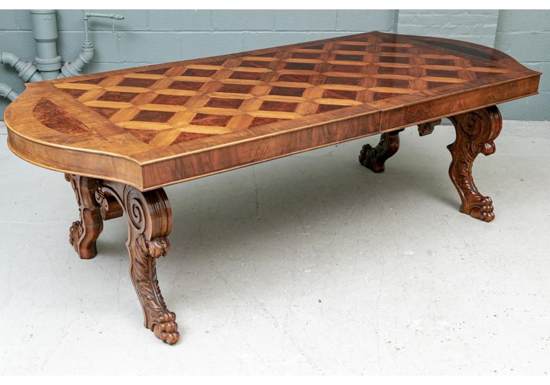 A large, substantial and very decorative Dining Table with a striking presentation. The exquisite banded top with a large parquet harlequin diamond pattern in darker figured wood and shaped ends. With a substantial frieze supported by heavily carved