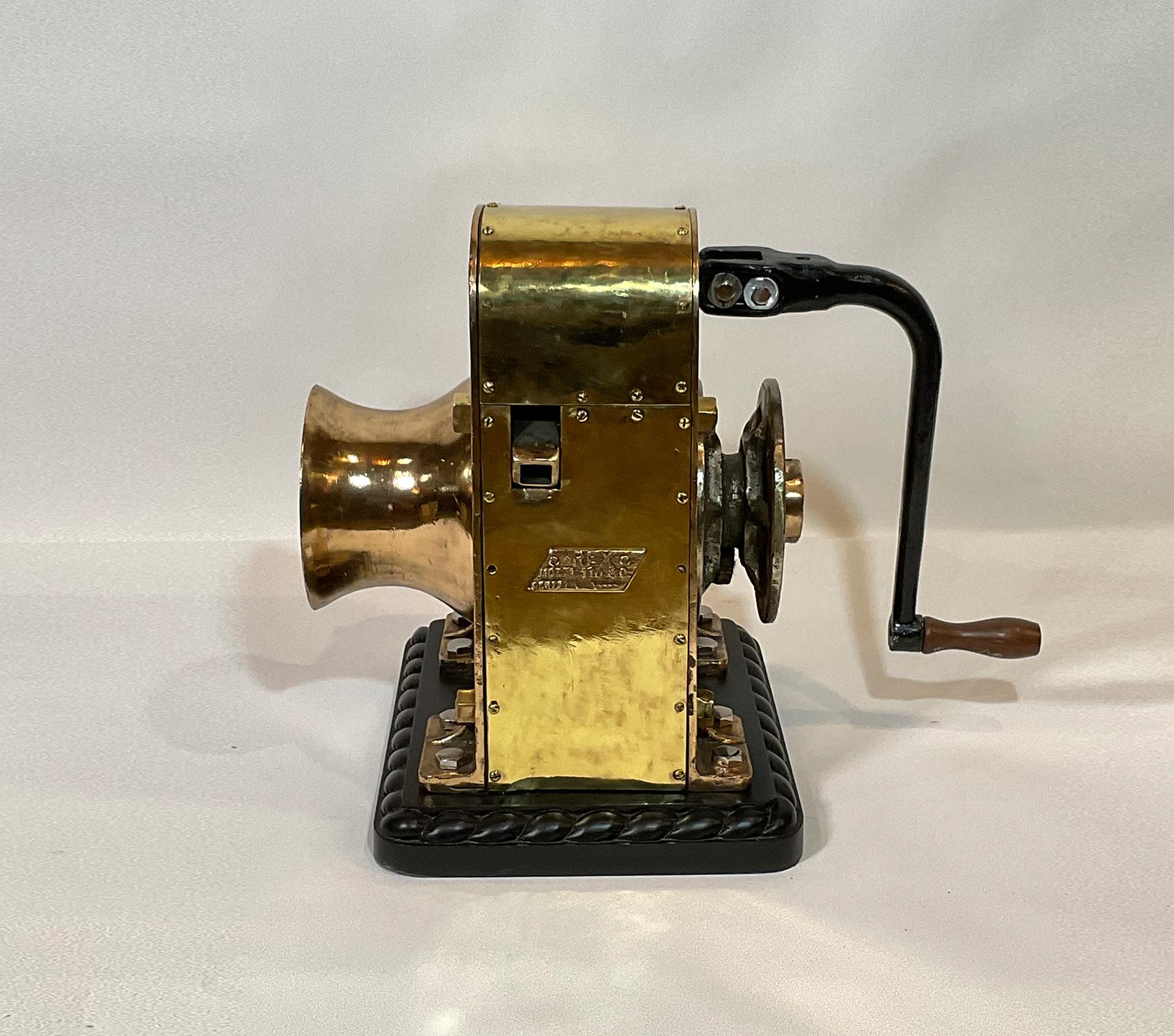 Ships winch by REX, model 110. This is extremely heavy, 220 pounds. The huge brass drum has a shaft that runs through the winch connecting to a chain sprocket. Also fitted with an iron handle with wood handle. Mounted by us to a wood base with rope