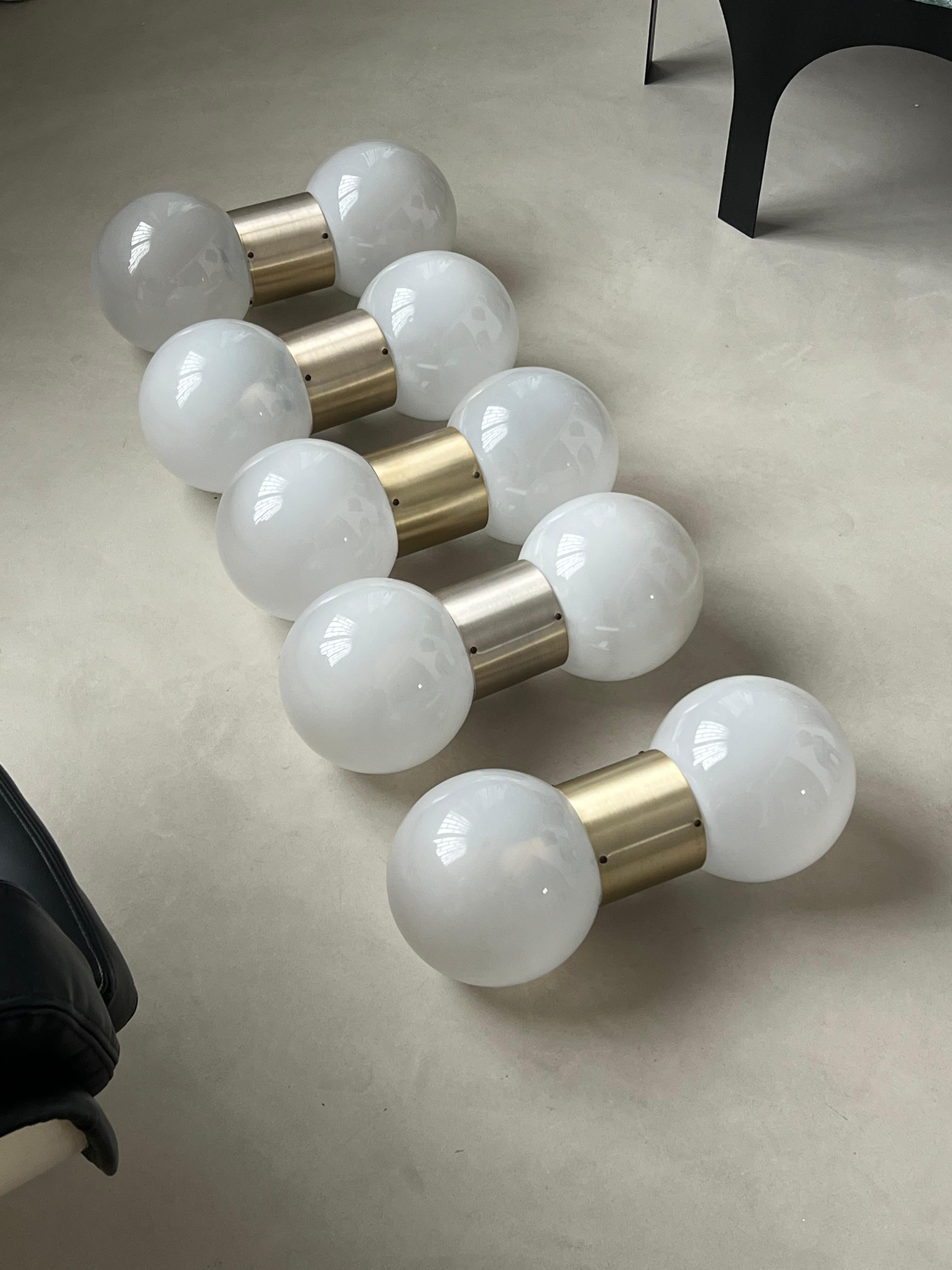 Massive, intramontabili ed eleganti applique di Stilux Milano degli anni Settanta, 
un corpo cilindrico in metallo fissato alla parete da un piccolo danno geometrico, alle due estremità si trovano due grandi sfere di vetro opalino bianco che creano