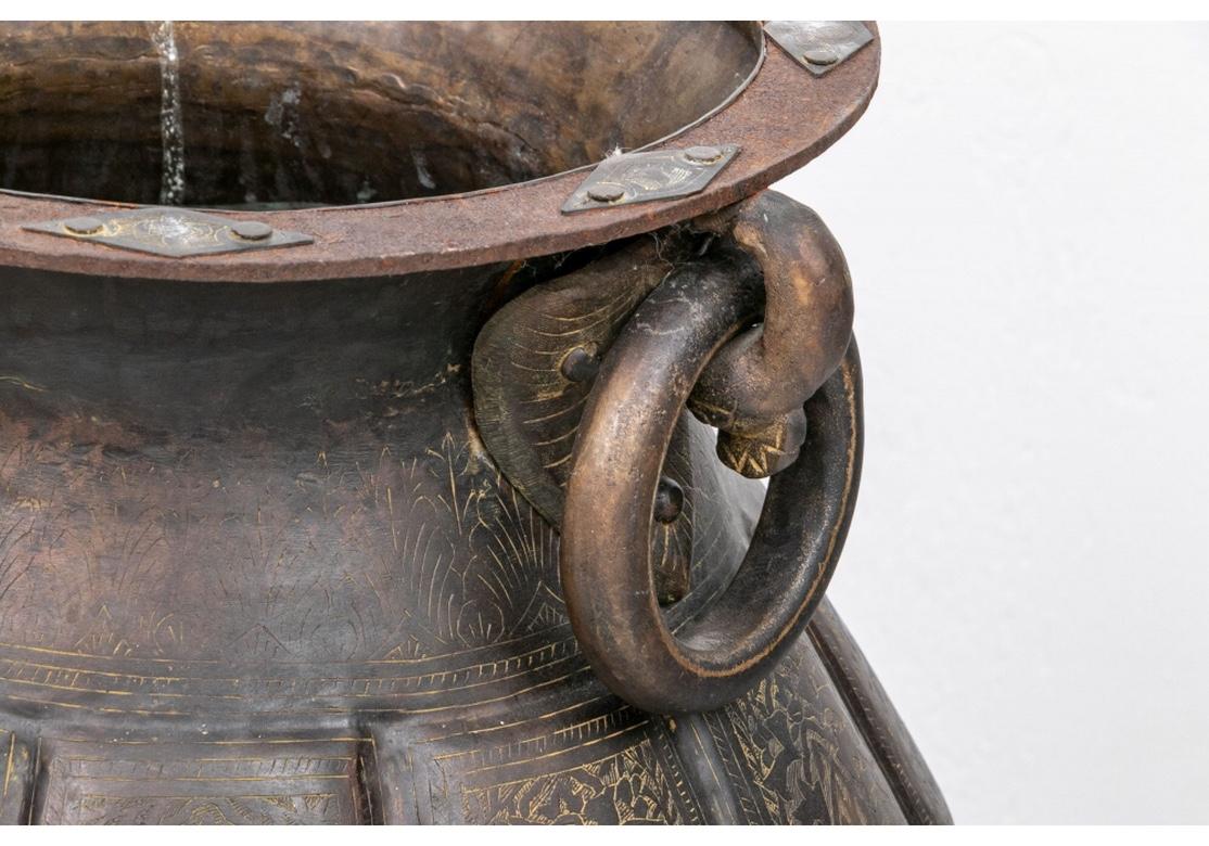 An older and massive age patinated brass footed urn with a bulbous form having relief scallop motif around the vessel and conforming base. The urn with bold 5