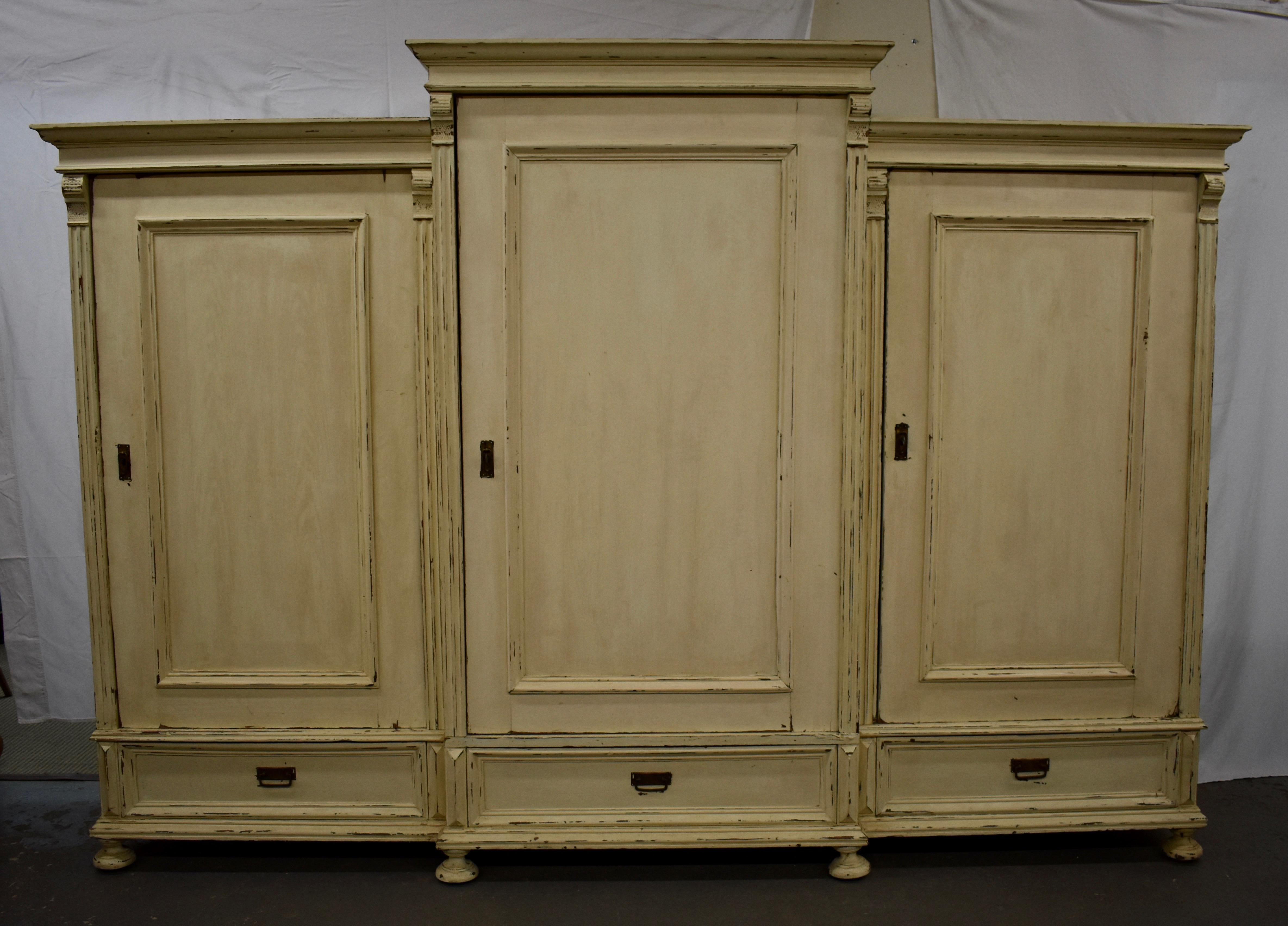 This huge piece is built as three one door armoires, the centre piece being taller and deeper than the sides creating a breakfront with a raised pediment. Each section has a single flat paneled door a deep hand-cut dovetailed drawer and has fluting
