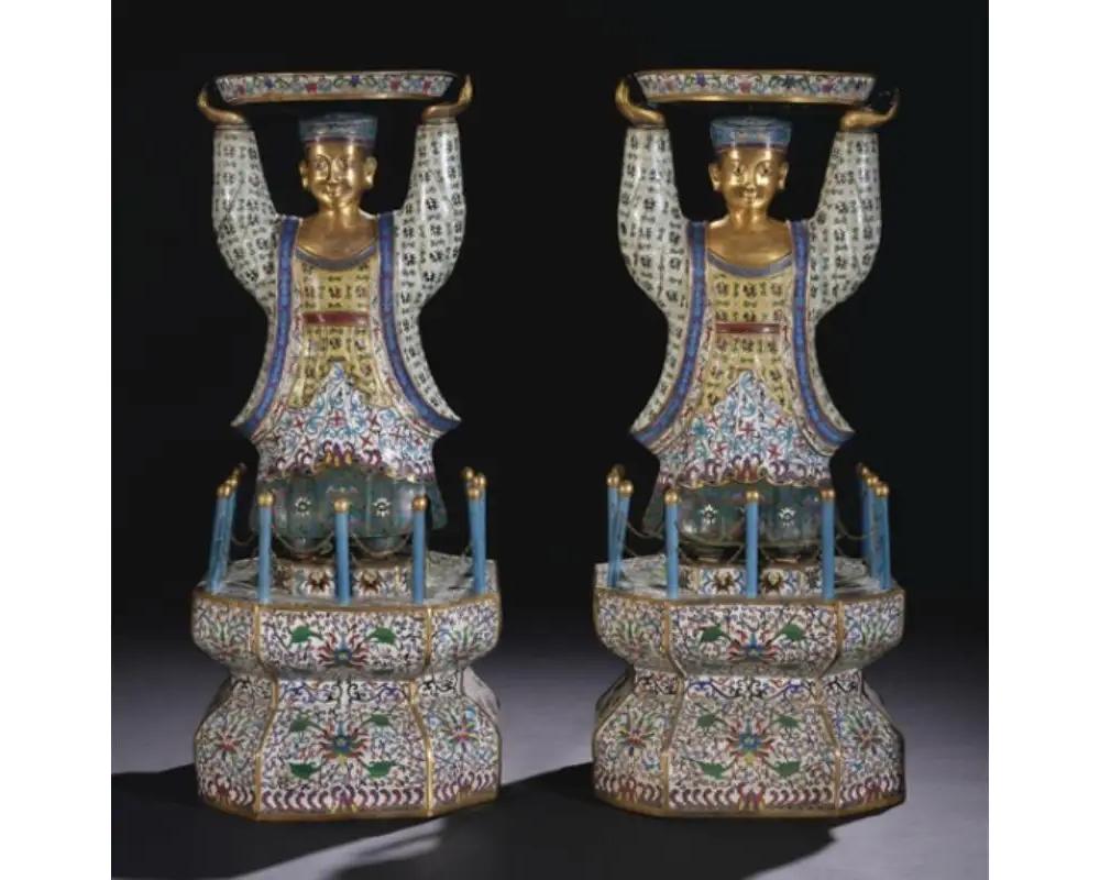 A rare and massive pair of Chinese cloisonne enamel figures of attendants, late Qing Dynasty.
 
Each standing figure similarly depicted with hands raised overhead supporting a large circular tray, all raised on a tall octagonal waisted stand