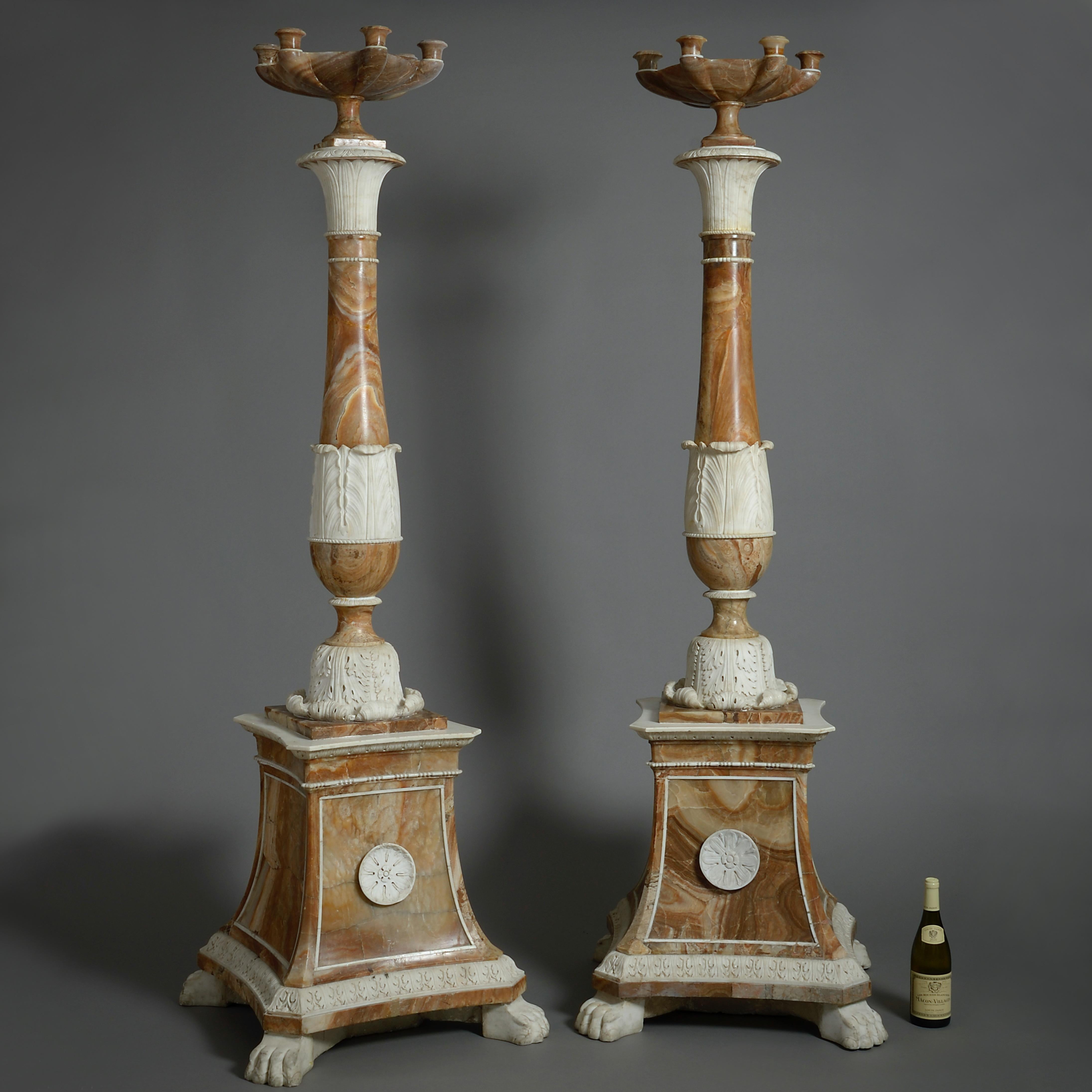 A MAGNIFICENT AND MASSIVE PAIR OF ROMAN STATUARY MARBLE AND TUSCAN ALABASTER TORCHERES, CIRCA 1800.

Each with a six-light tazza form candelabrum atop a shaped column with stiff-leaf capital and acanthus-carved socle on a panelled square spreading