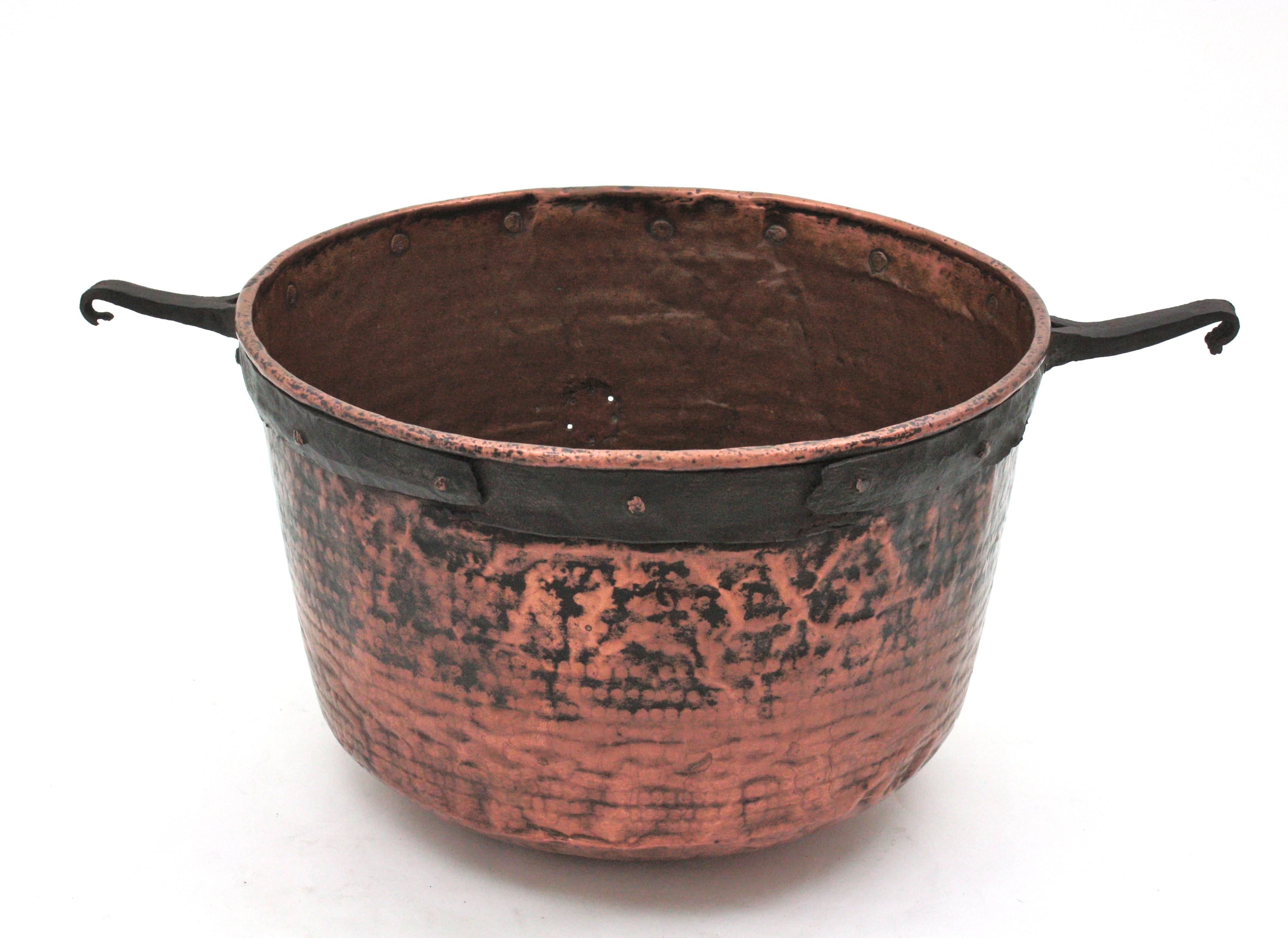 Oversized hand-hammered copper cauldron with iron hook handles. Spain, early 20th century.
This handcrafted copper cauldron has a terrific aged patina. It has an iron rim on the top and forged iron hook handles attached to the cauldron with copper
