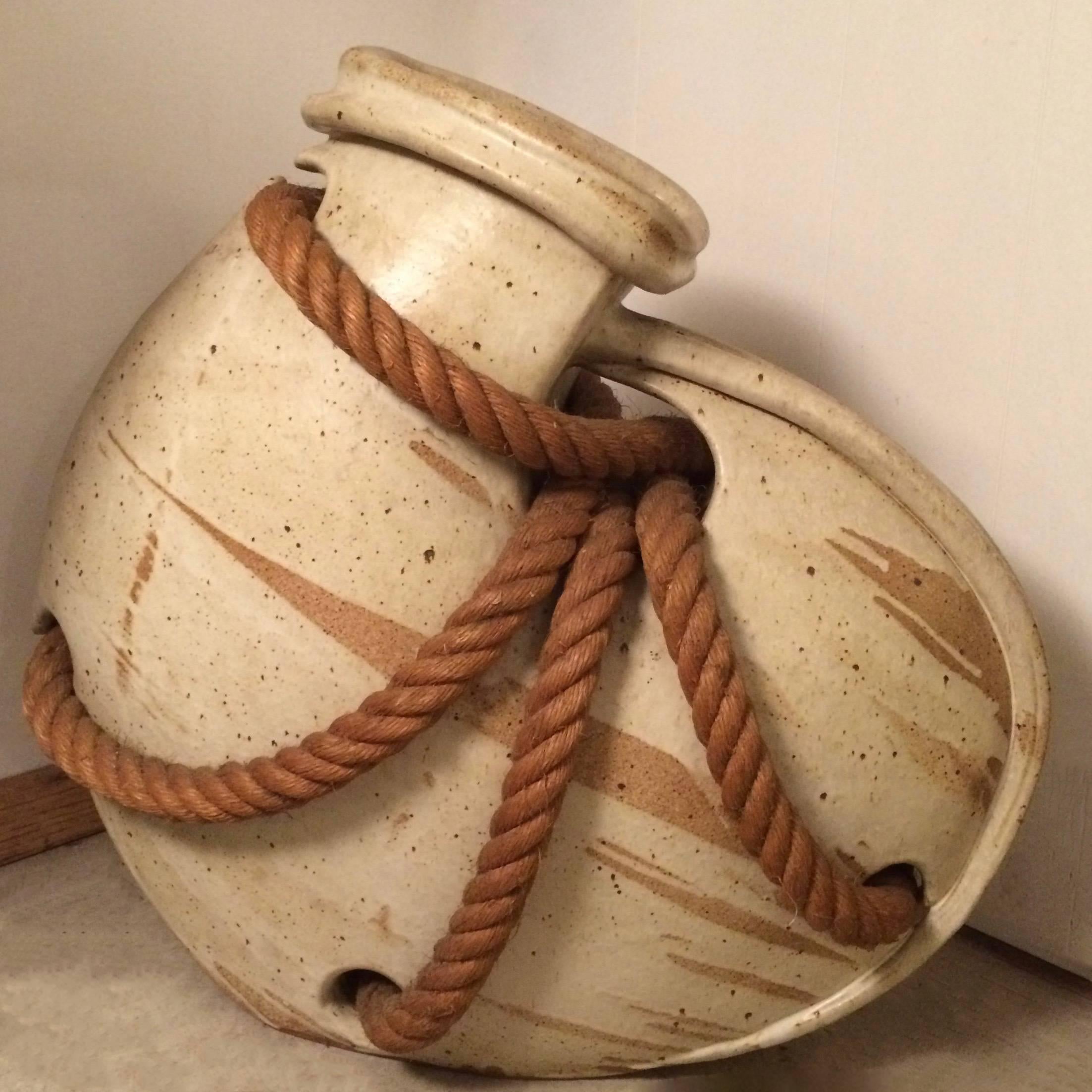 Massive, ovate shaped, studio pottery vessel, swathed in thick nautical rope is signed on the bottom “Hammer”. The vessel features interesting organic lines with striated tan on beige, satin glaze. The vessel is a truly impressive show piece.