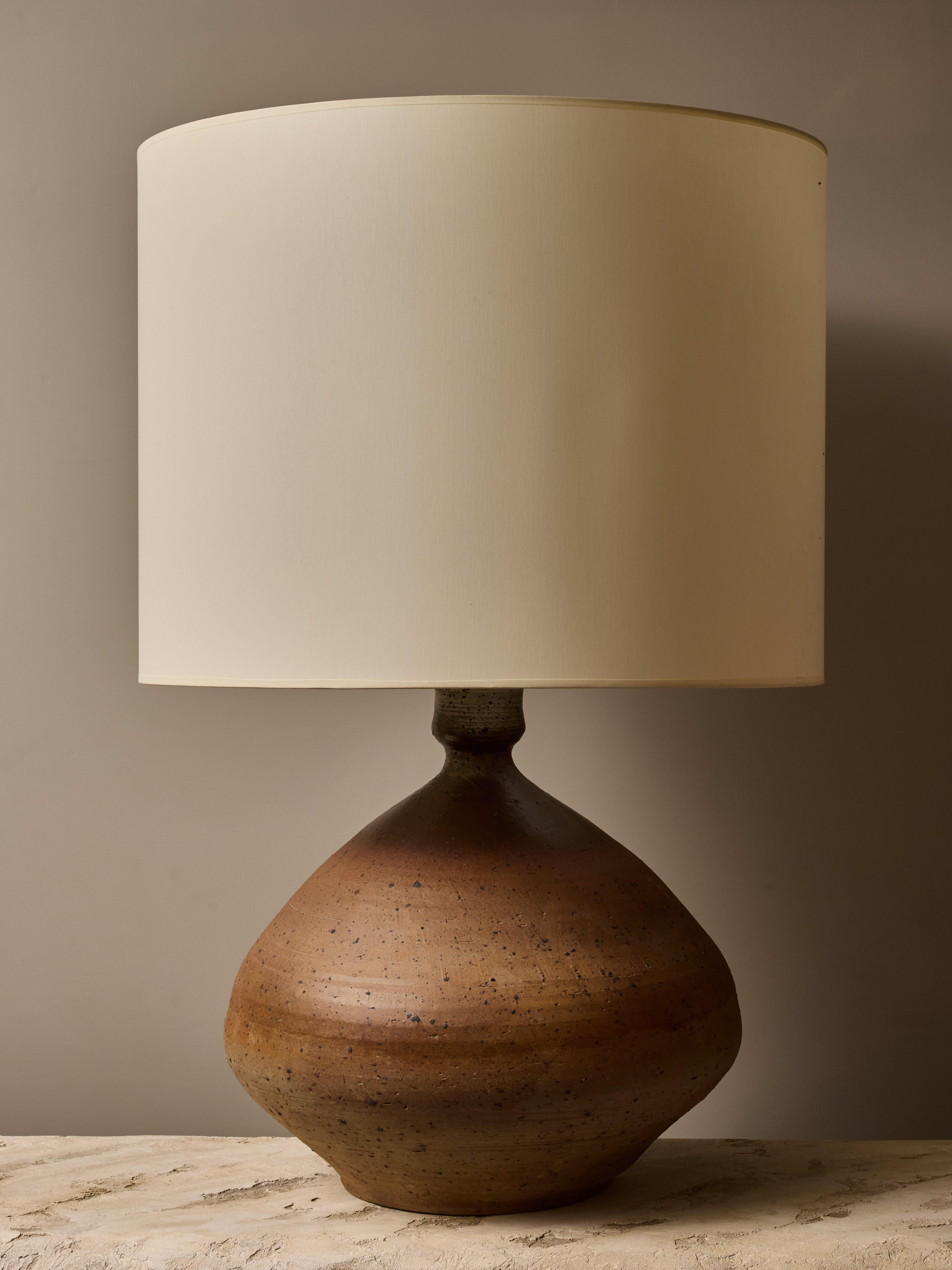 Très bel exemple des premiers travaux de François Lanusé, cette grande lampe de table en céramique aux tons très terreux s'estompe du bas vers le haut, avec des mouchetures sombres tout autour. Surmontée d'un grand abat-jour neuf, cette lampe peut