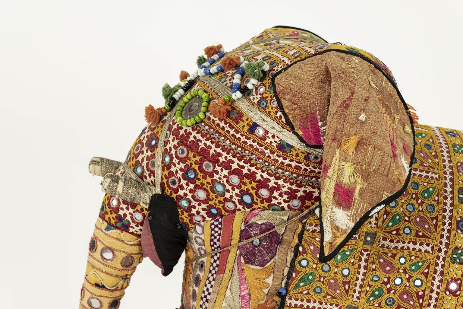Massive vintage cotton elephant, covered in Indian textiles, retailed in the 1950s by Harrods. Exterior decorated in embroidered designs, tassels, tiny mirrors, beads, metallic trim and a brass bell. Interior frame composed of wire and straw.