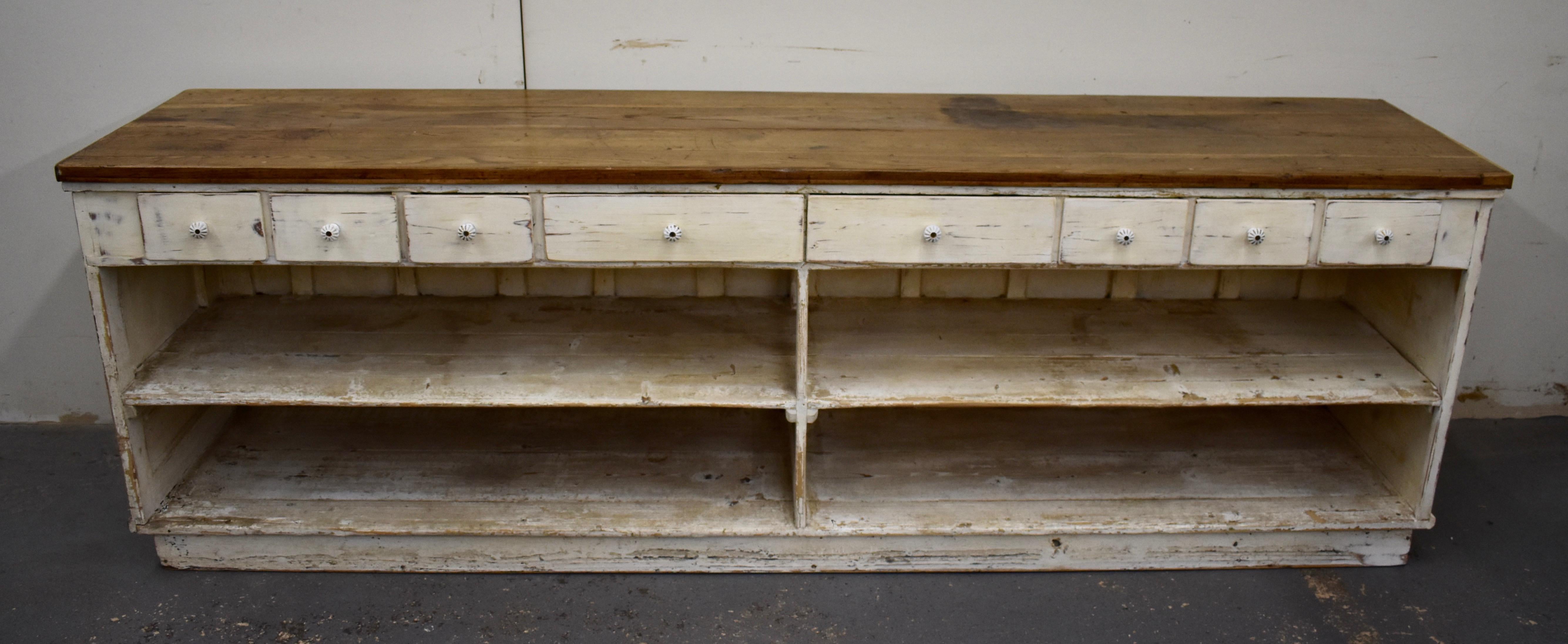 This is a huge vintage store counter with a pine base, one side of which is entirely plain except for four applied corbels. The other, the storekeeper’s side, is open with eight drawers with ceramic knobs along the top apron and a deep storage