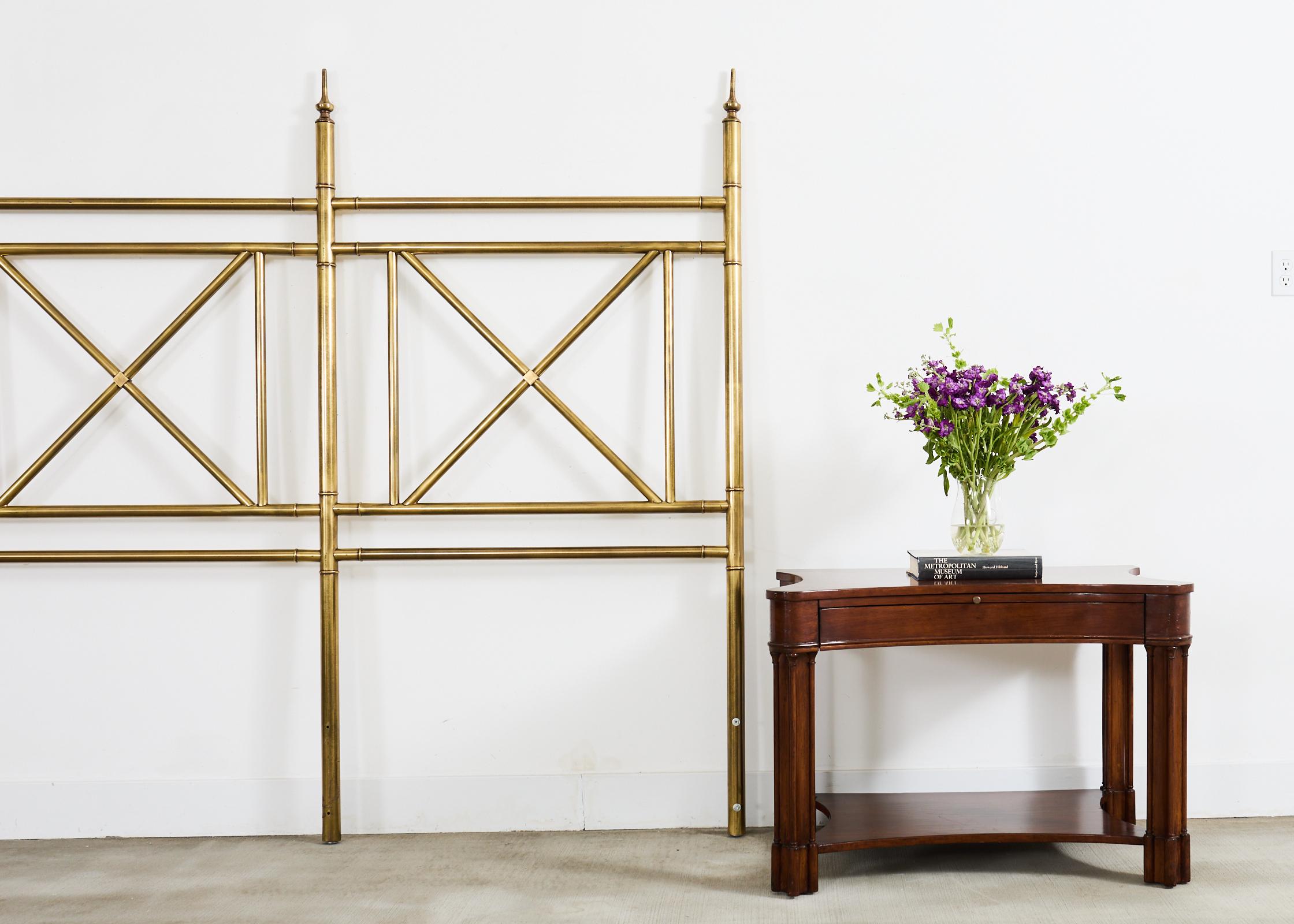 Mid-century modern king size brass headboard made in the manner and style of Mastercraft. The large headboard features a faux bamboo brass frame featuring neoclassical style x-form stretchers. The bed frame has three supports ending with decorative