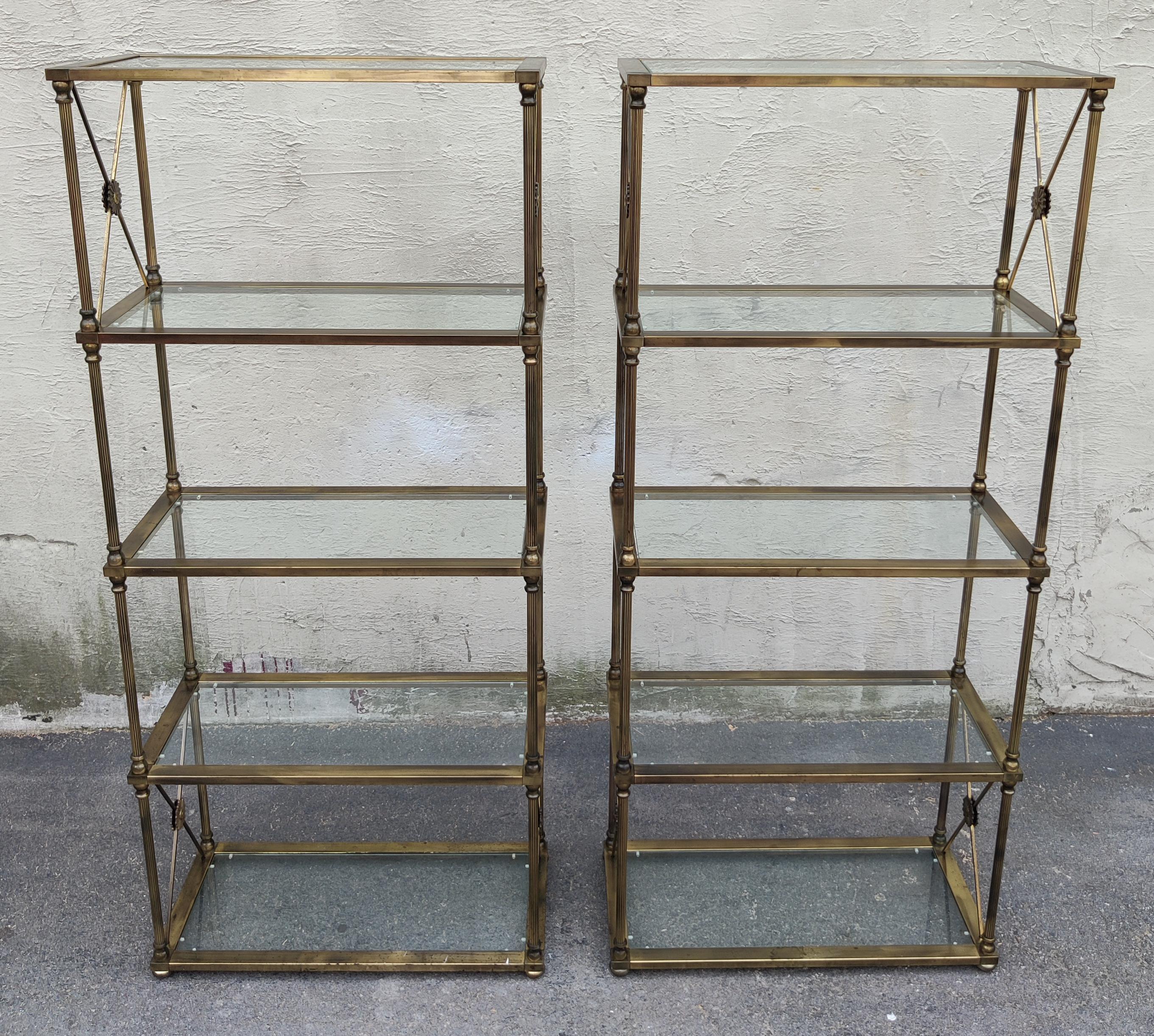 This pair of brass and glass etegeres were made in the style of distinguished manufacturer Mastercraft, and feature high quality construction and classical design touches. These include fluted brass supports in each corner and ornate solid brass