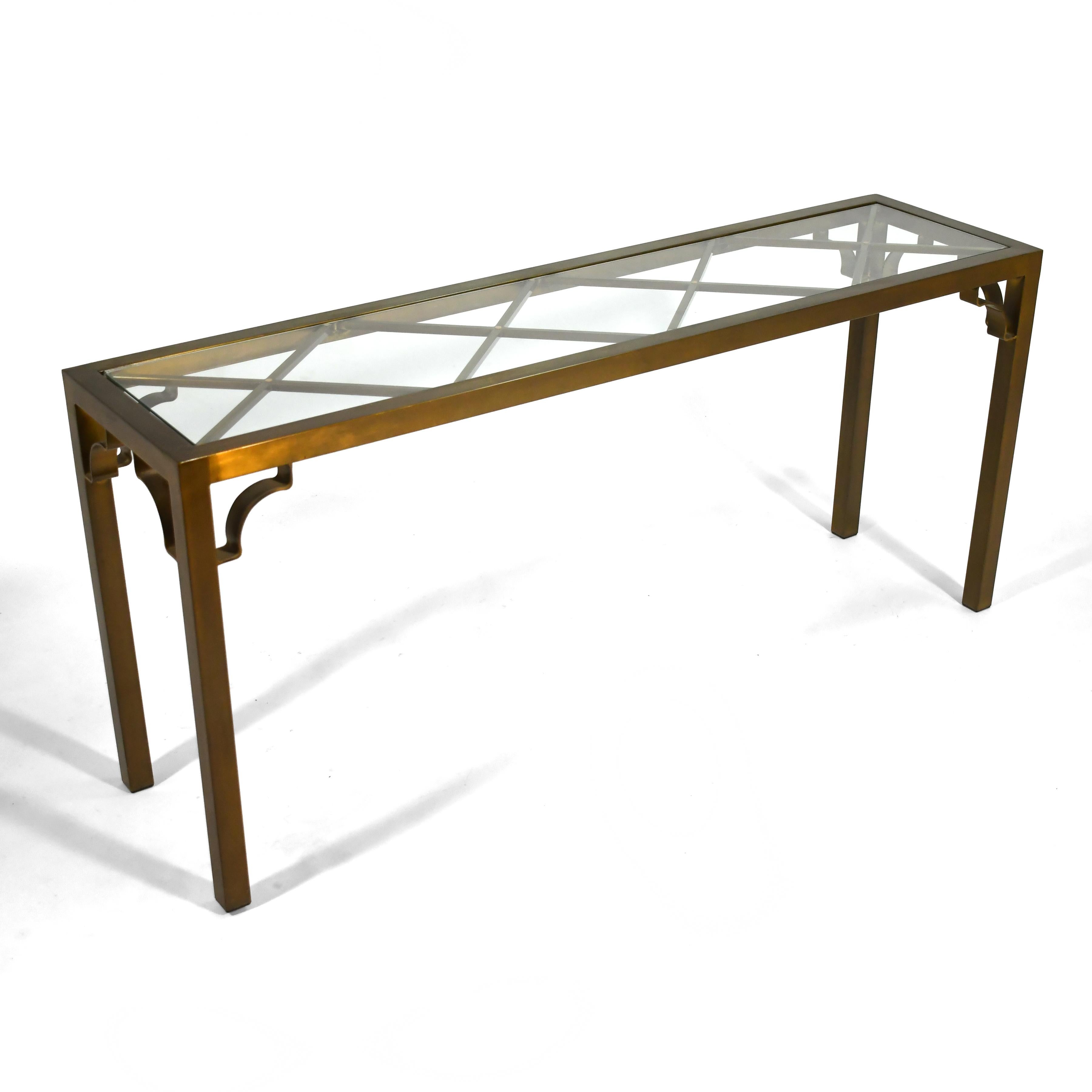 This console table by Mastercraft features a simple parsons table form that is nicely detailed with a diamond lattice design supporting the glass top and open Chinoiserie brackets in the corners. The entire table has a rich antiqued brass