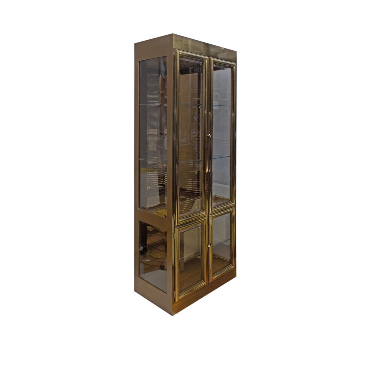 A midcentury brass and glass display cabinet / vitrine by Mastercraft, USA, circa 1960. Featuring two upper and two lower glass panel doors with glass shelves and interior lighting.