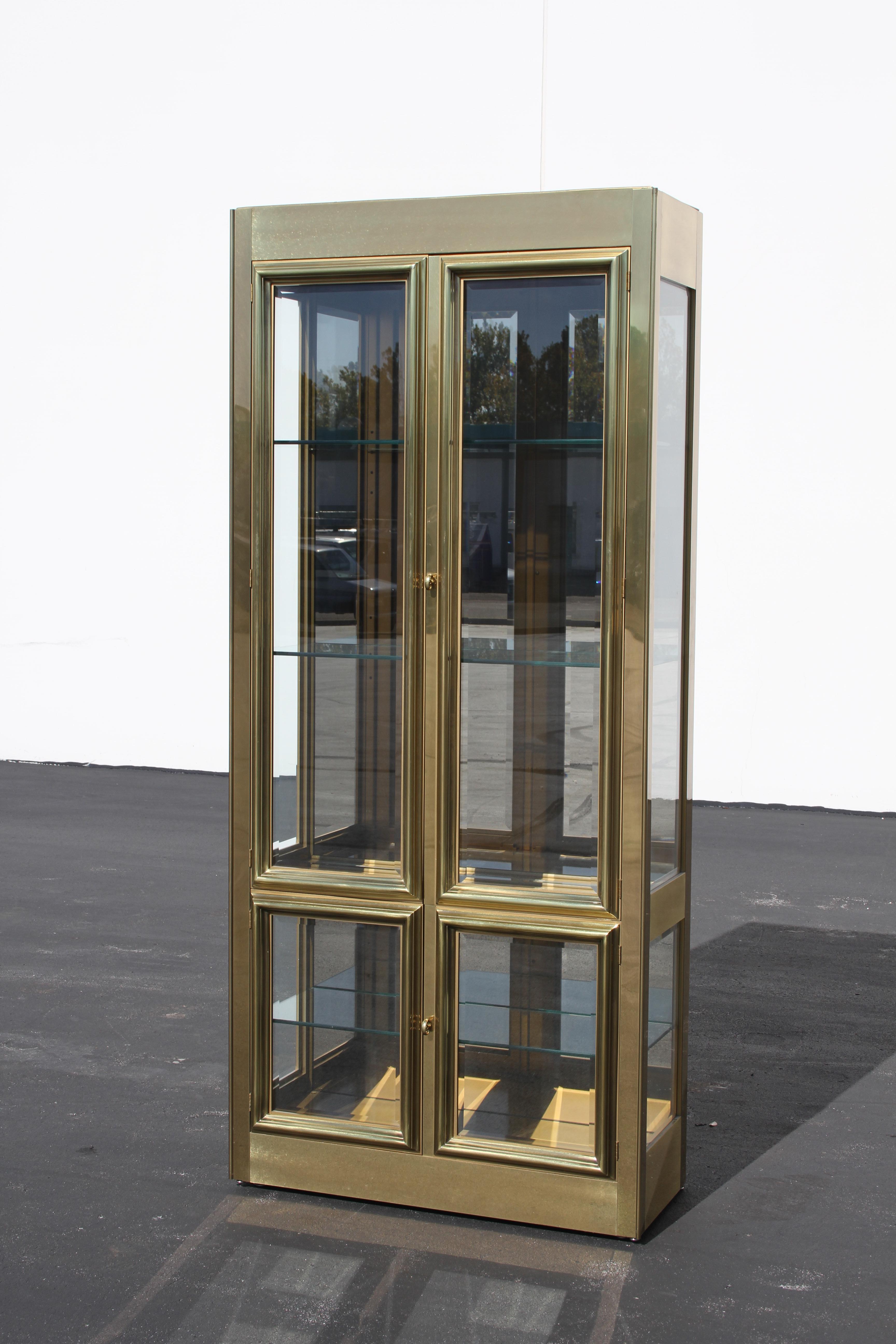 Mastercraft brass display or Vitrine with four beveled glass doors, design is circa 1970s, this was manufactured in the 1980s. Has three adjustable glass shelves and mirrored backing. Ceiling has two internal lights, switch and cord. Upper case with