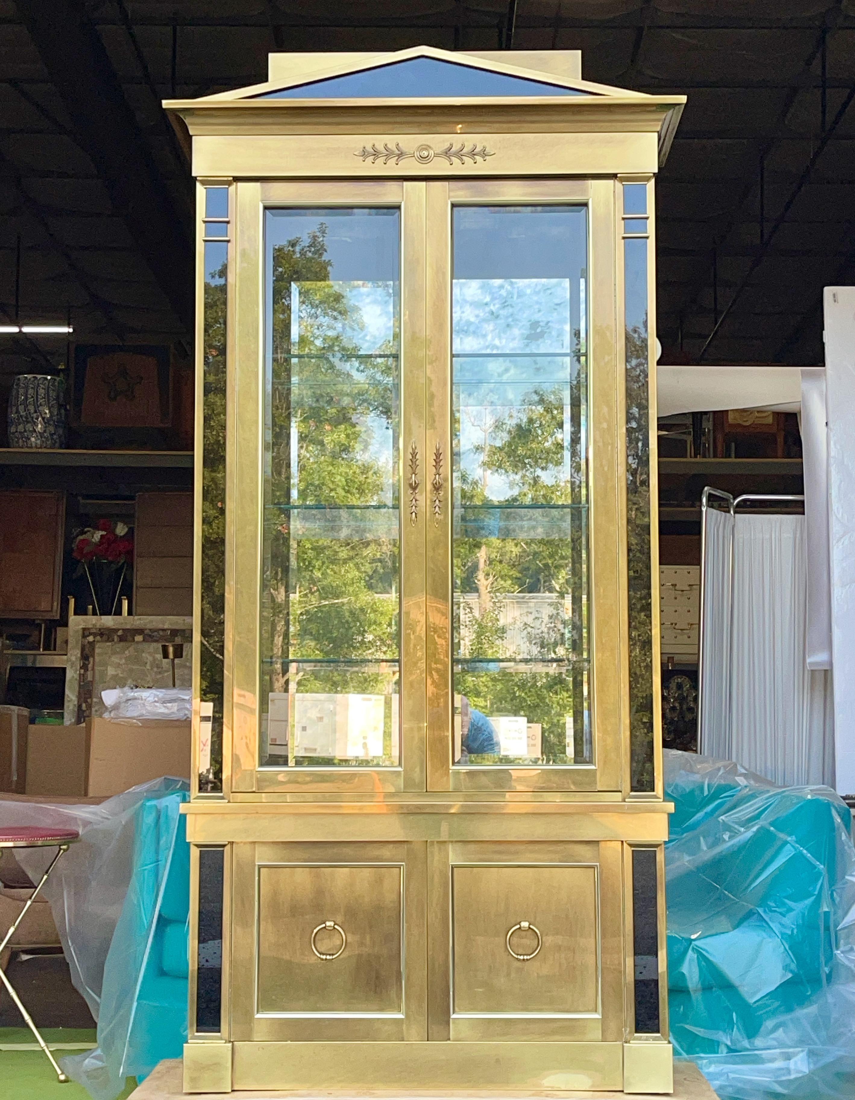Mastercraft model 260 'China Cabinet' or vitrine, display cabinet, curio in the empire style with pediment.
Hardwood structure clad in patinated solid brass and black mirror trim.
Beveled glass sidelights and windowed doors. Storage cupboard behind