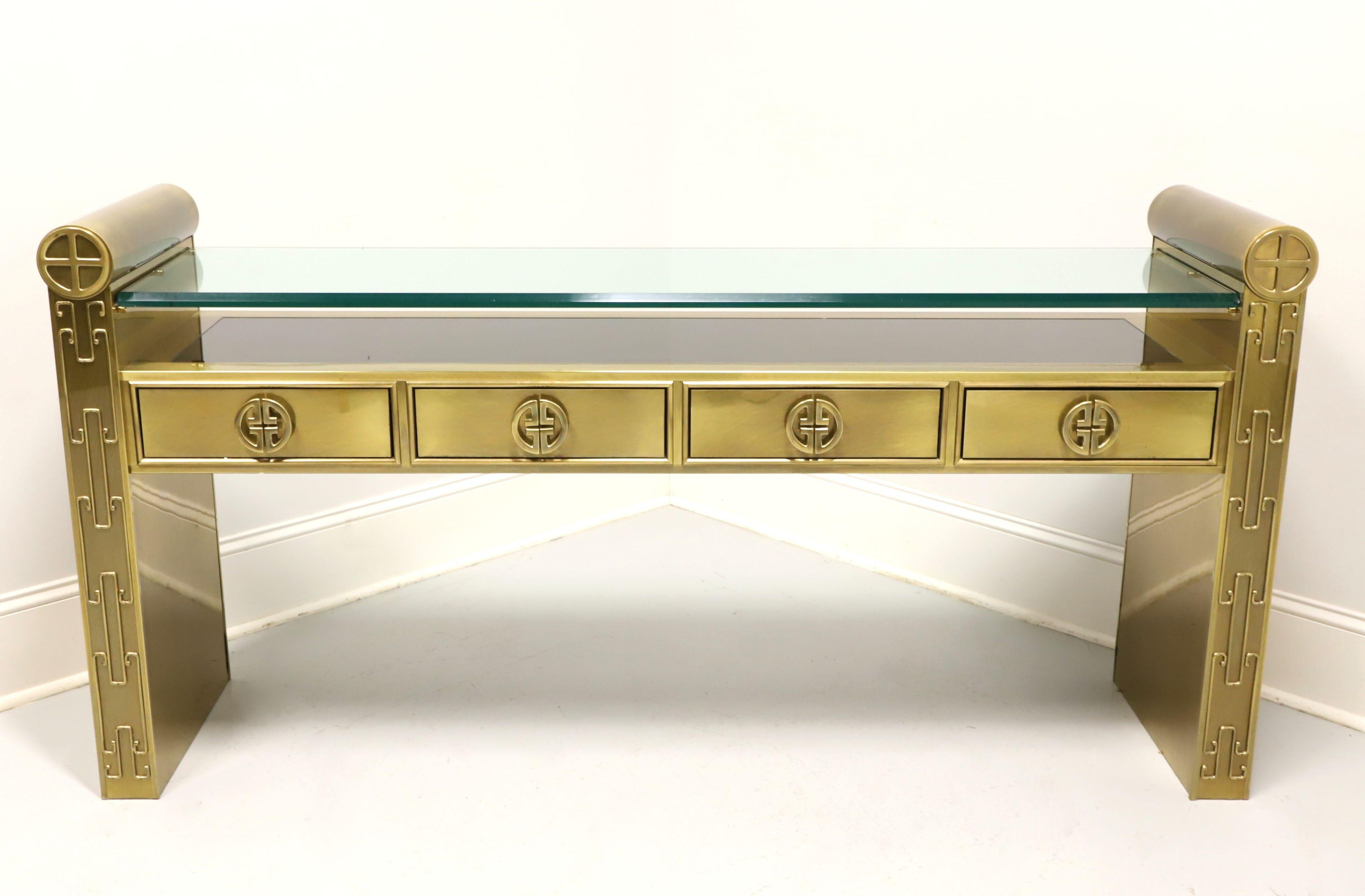 An Asian style console table by Mastercraft. Wood frame with a solid brass overlay, glass top with bevel edge, black display shelf under glass top, Chinoiserie pattern adornments, decorative brass drawer hardware, smooth rounded tops to the sides,