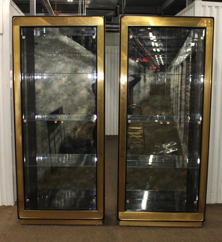 Stunning pair of 1970s Mastercraft brass vitrine cabinets with black lacquered frame and antique mirror backing, with two overhead light with dimmer and 3 glass shelves.