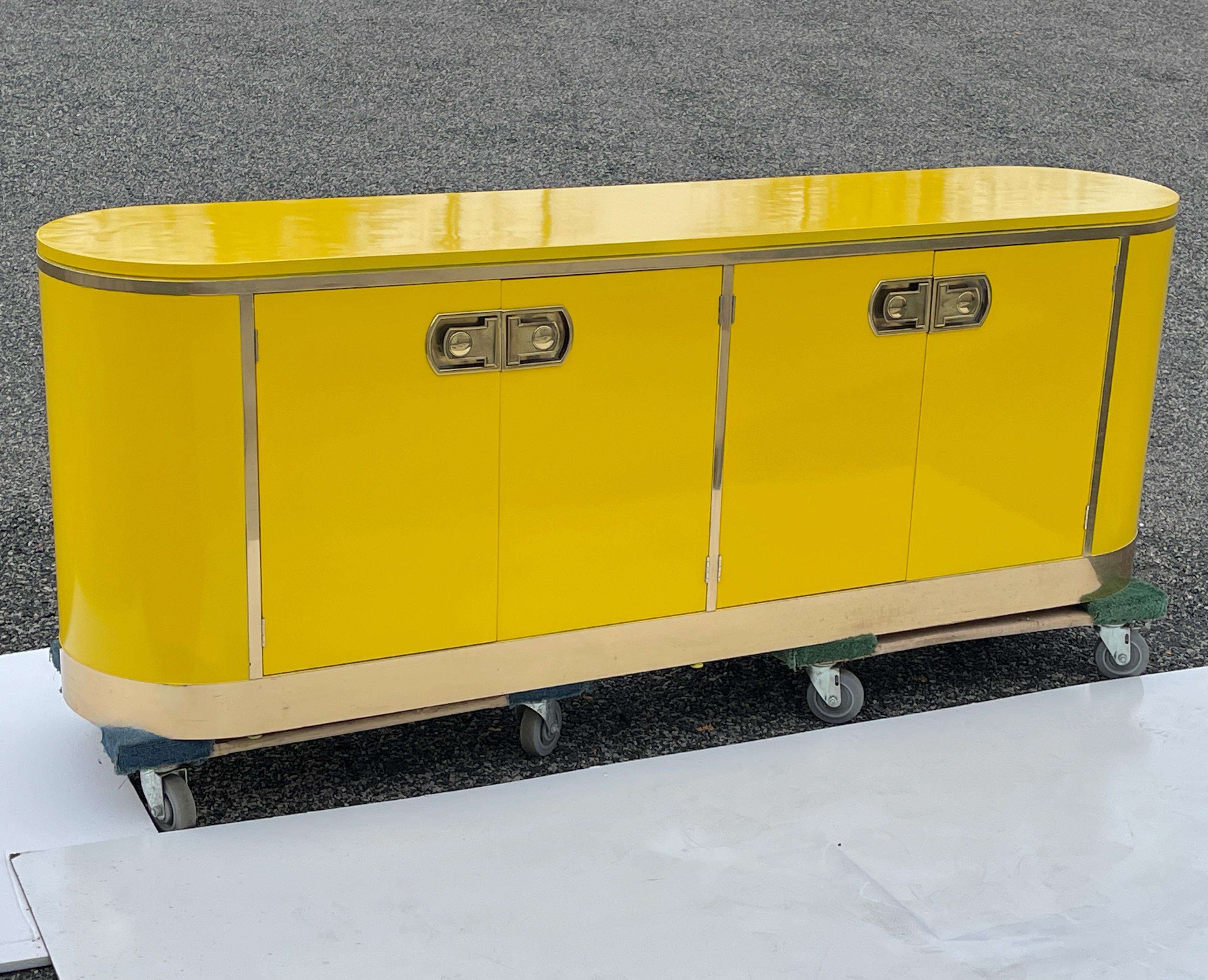 Mastercraft of Grand Rapids '1565' racetrack oval shaped buffet cabinet designed by William Doezema in 1974 newly refinished in high gloss yellow lacquer with four doors and embellished with polished solid brass trim and wrapped base. 
Solid