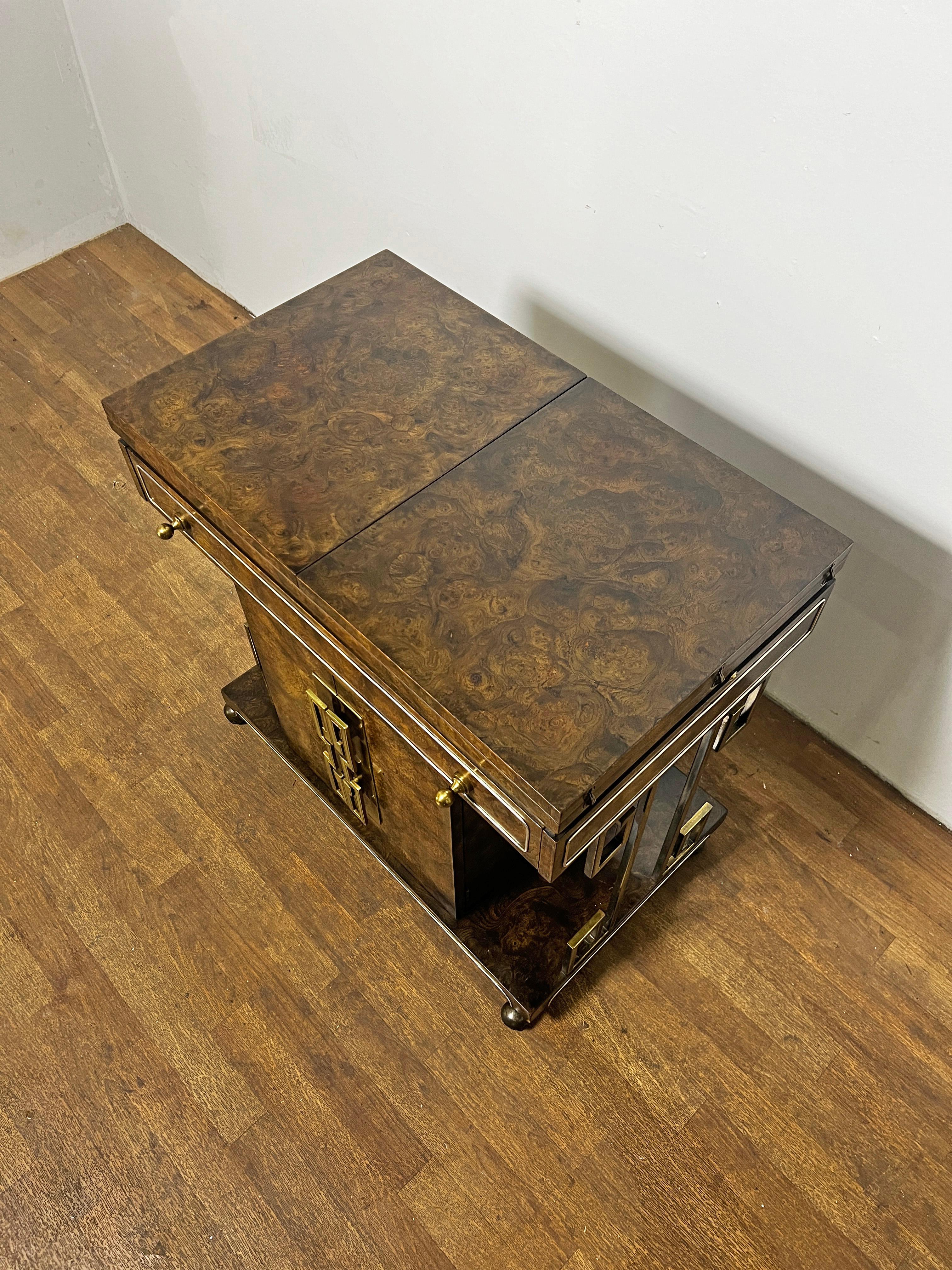 A 1960s drinks trolley bar cart with expandable top and additional storage below and at sides, in burl wood with brass greek key accents, designed by William Doezema for Mastercraft.

Measures 30