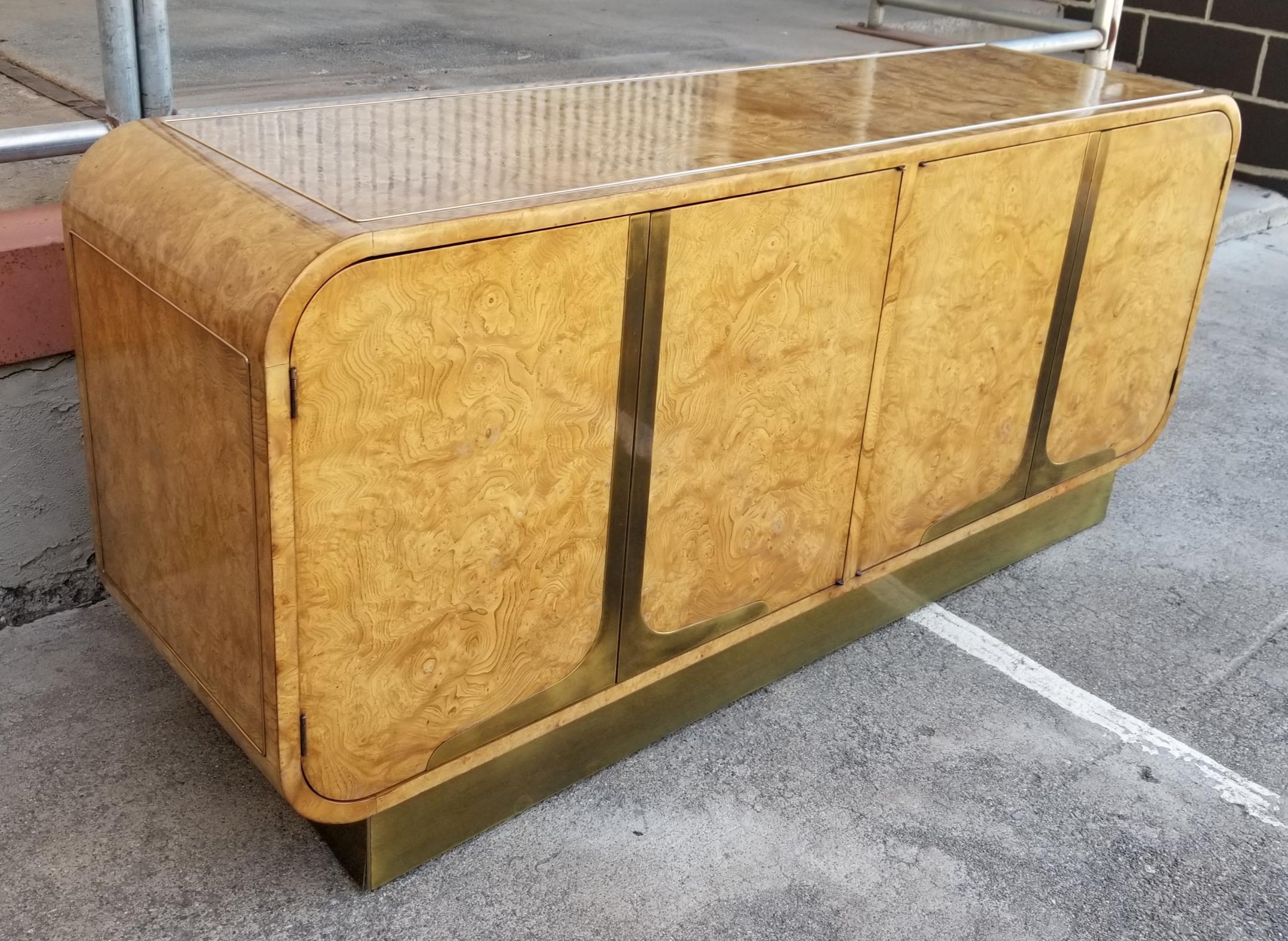 Striking, exotic burl-wood credenza with brass detail. Push and release doors with fitted interior. Mounted to a brass plinth with beautiful curvaceous corners. Designed by Wiliam Doezema for Mastercraft Furniture.