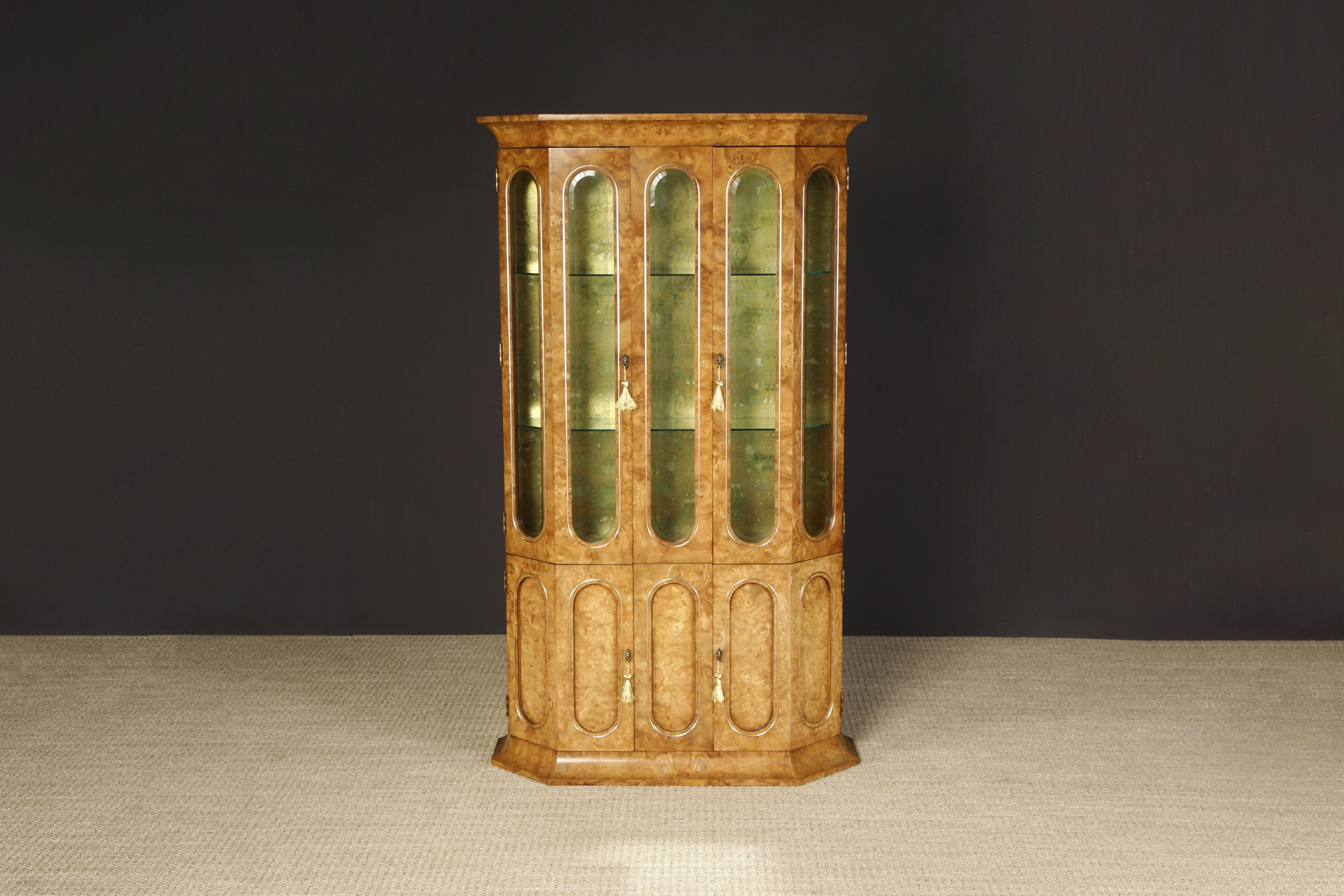 This incredible burled wood display cabinet, produced by Mastercraft in the 1970s, features incredibly exotic grained burl with arched glass display windows, illuminated interior, exquisite antiqued interior, and interior glass shelves which are