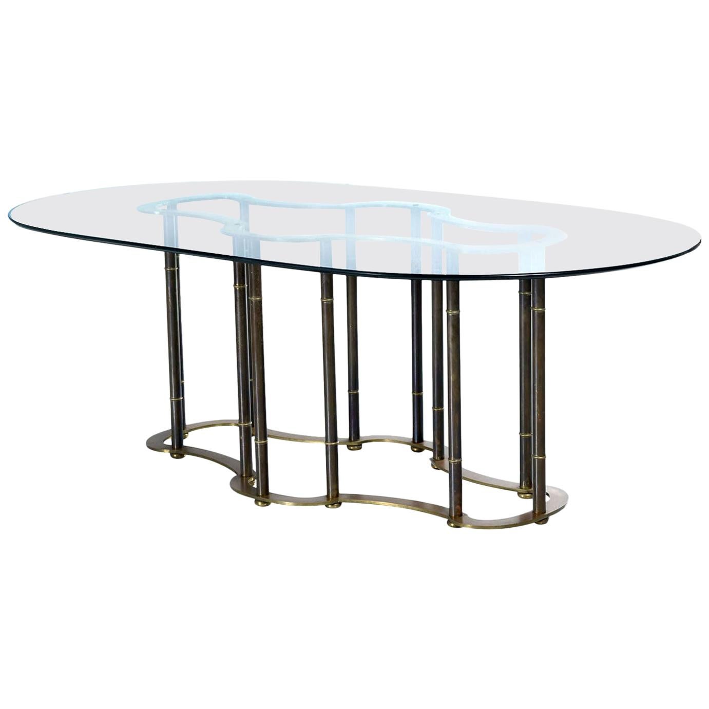 This expertly embodied faux bamboo brass dining table proudly wears its over four decade old patina. The patina gives the otherwise gold colored brass a dark, black bamboo look. The top of the table pedestal resembles a racetrack. The undulating