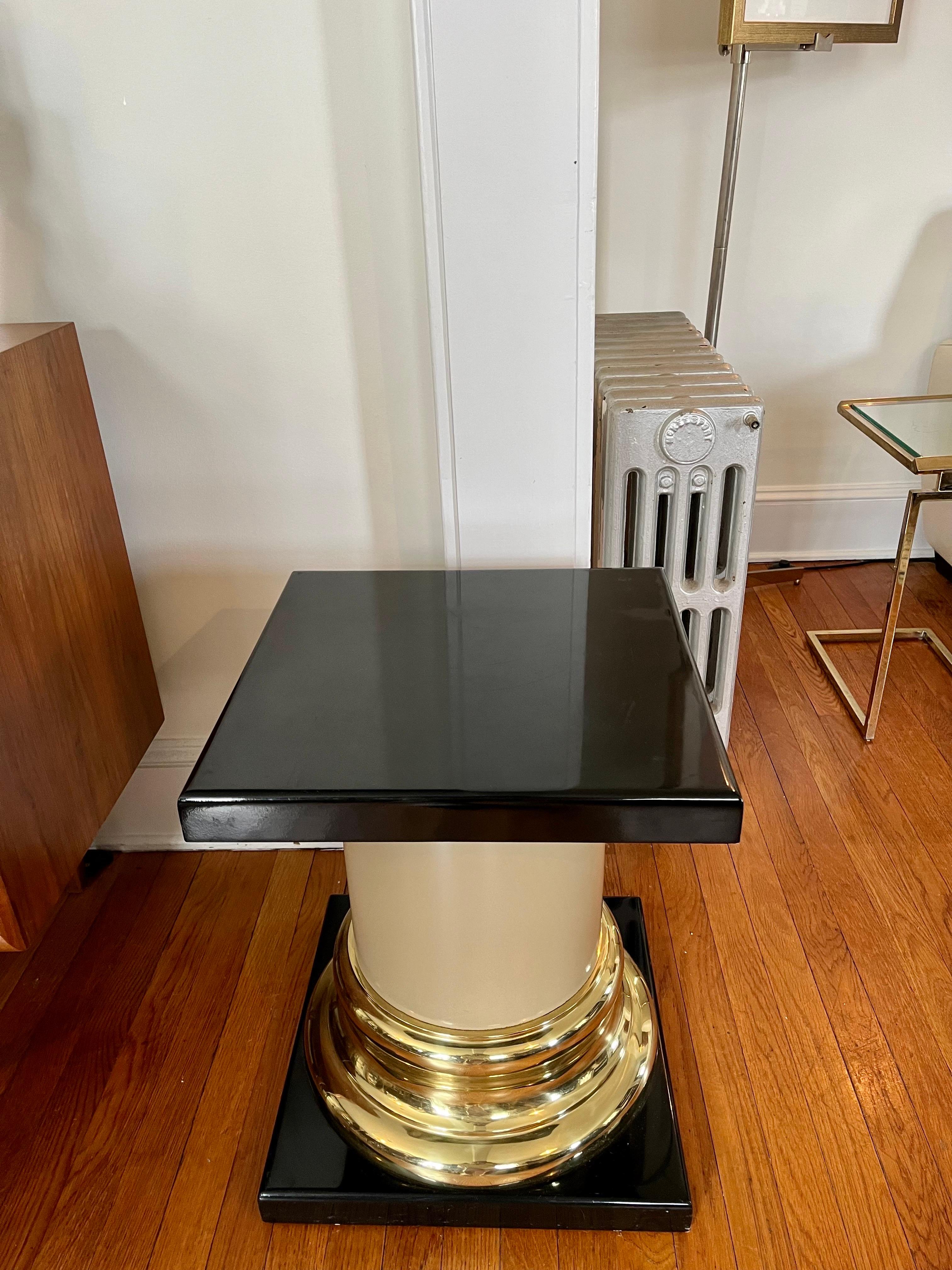 A Mid-Century Modern Mastercraft pedestal or side table with a simple Roman Tuscan column design. Featuring a smooth cylindrical latte colored resin (or ABS plastic) shaft with solid brass capital and base terminating on both ends in a satin black