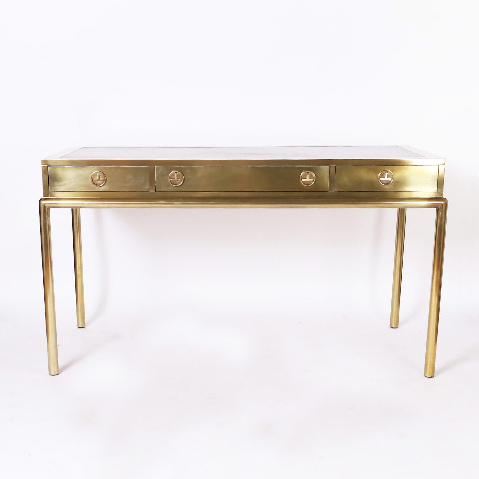 Now a modern design classic, a signed Mastercraft brass desk having a sleek no nonsense form, tooled brown leather top, a case with three drawers having stylized campaign hardware and four elegant tubular legs.