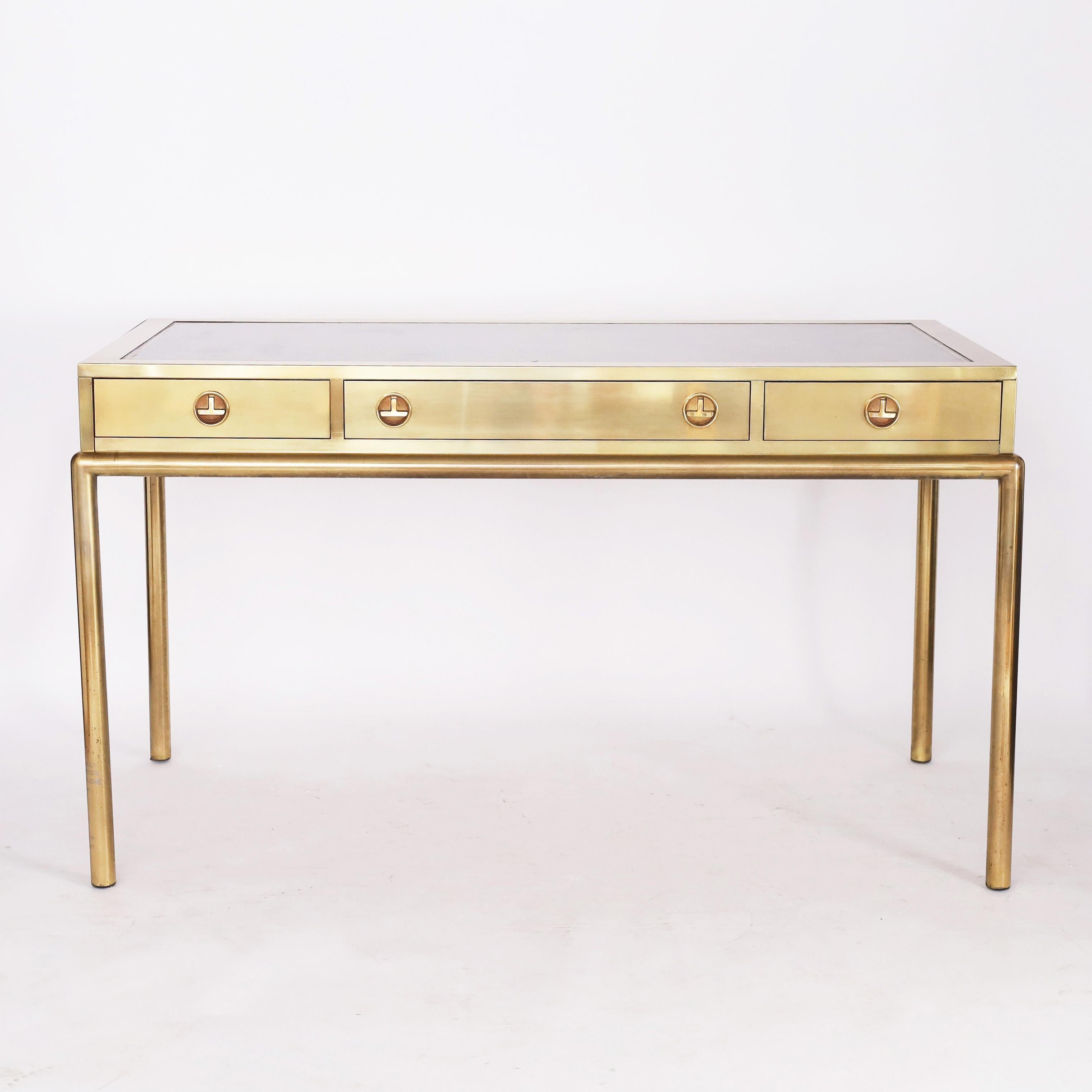 Impressive vintage Mastercraft writing desk crafted in brass, in a sleek chinoiserie stylized form, with a unique acid washed finish, having a tooled leather top on a case with three drawers with modernized campaign hardware over elegant tubular