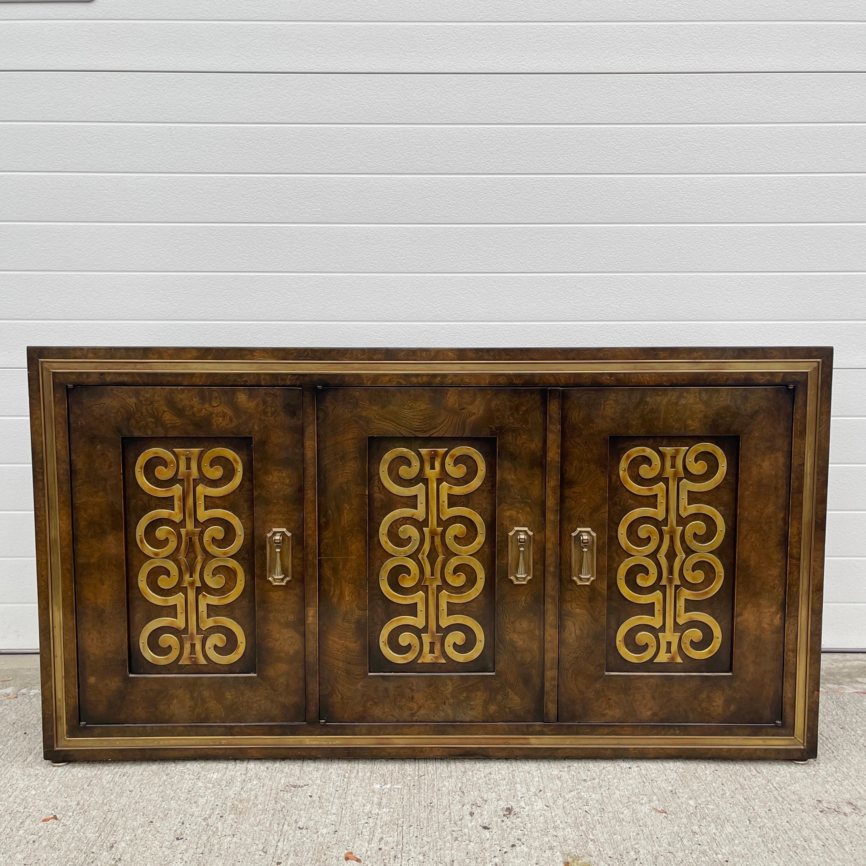 Mastercraft sideboard cabinet of drawers made from beautifully figured Carpathian elm with decorative brass appliques on three doors and brass trim around the outer edges.  The door on the left opens to an open cupboard space. The pair of double