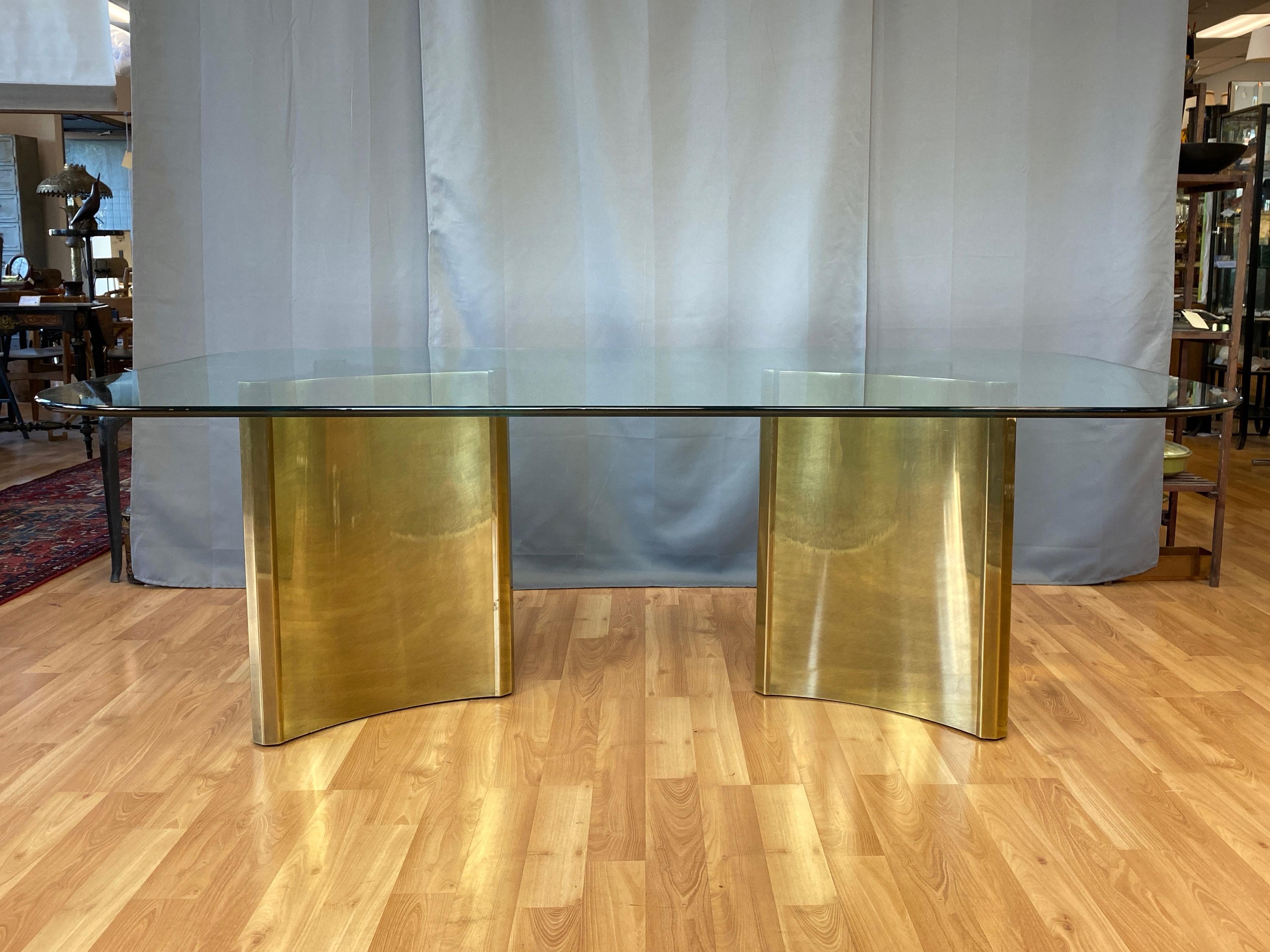 A monumental and rare Mastercraft Trilobi model 1972 brass pedestal base dining table with original glass top.

Striking pair of parabolic triangular pedestals are equal parts architectural and sculptural, with a chic yet commanding presence.