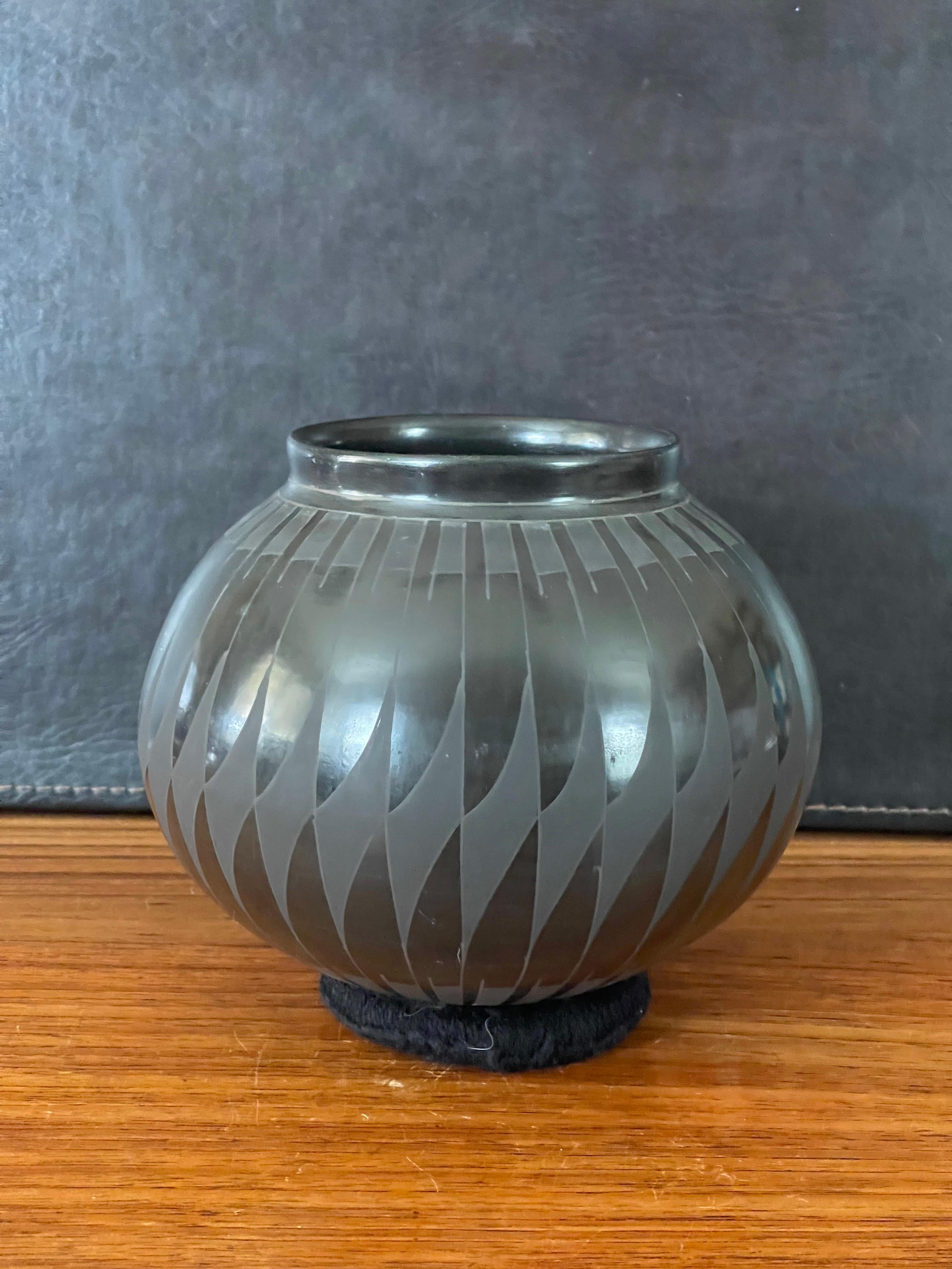 Magnifique vase géométrique en blackware tourné à la main par David Ortiz, vers les années 1990. Cette pièce exquise en argile naturellement noire présente un motif géométrique unique. Ce vase est en très bon état et mesure 7