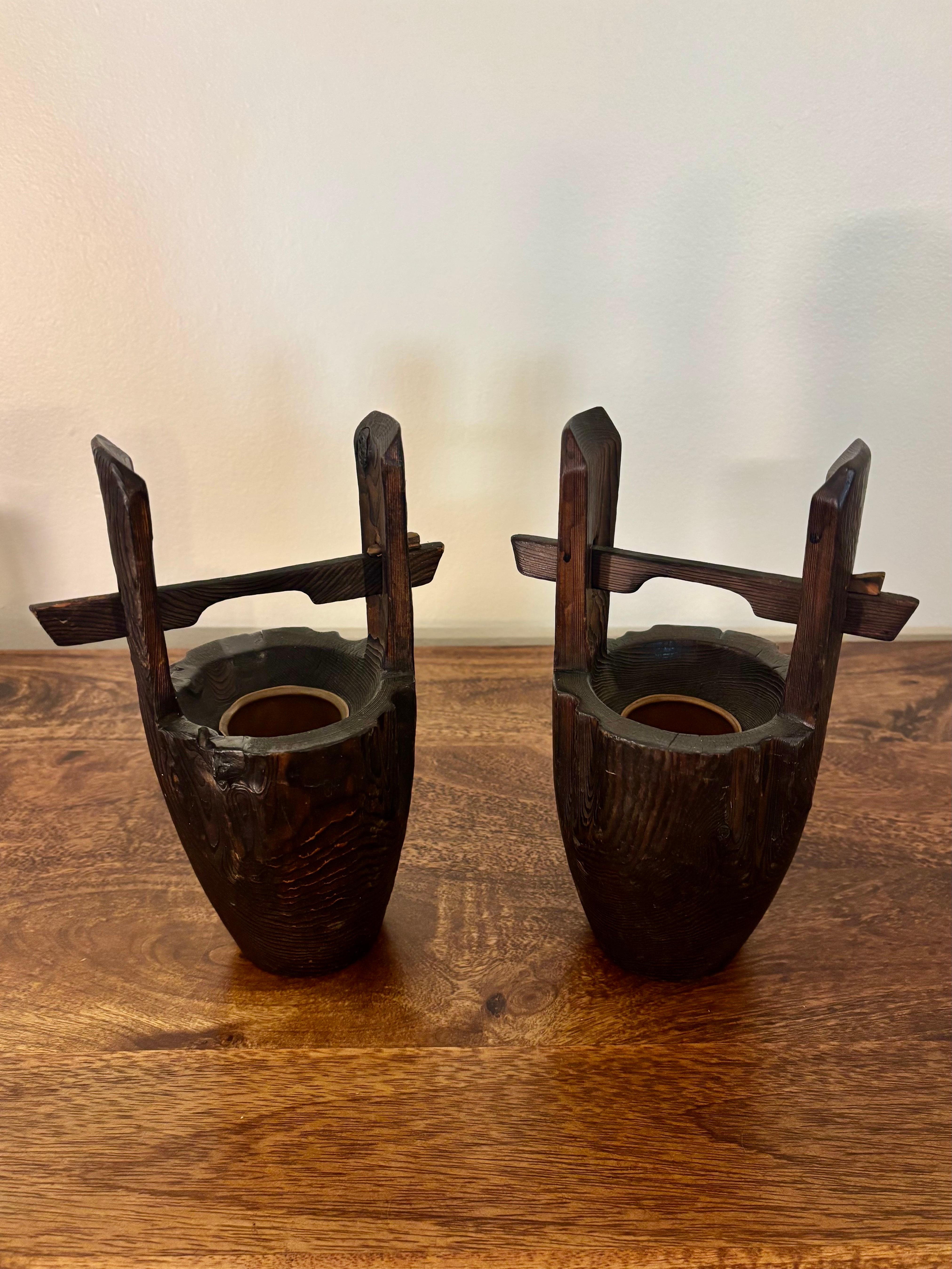 
Una raffinata e scultorea coppia di antichi vasi giapponesi Ikebana, ciascuno realizzato in legno con finitura scura e una superficie ricca di texture naturali. I vasi presentano una forma architettonica distintiva: un contenitore centrale in legno