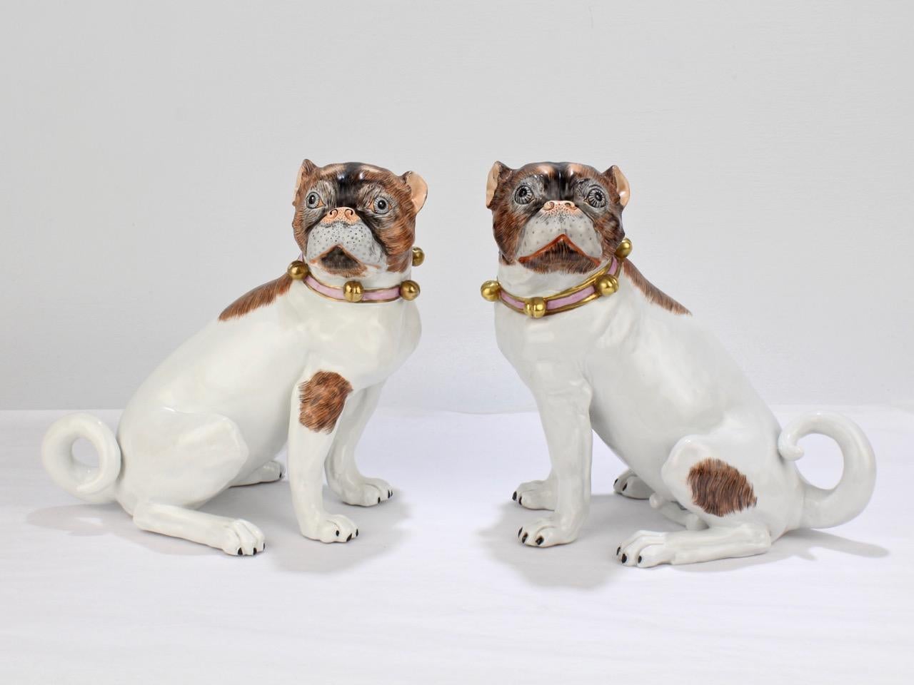 A fine pair or complimentary Dresden porcelain pug figurines.

Modeled as a matched pair, one is female and the other male. 

Each is decorated in brown and black paints, and bears a collar with bells.

The underside of each bears a blue