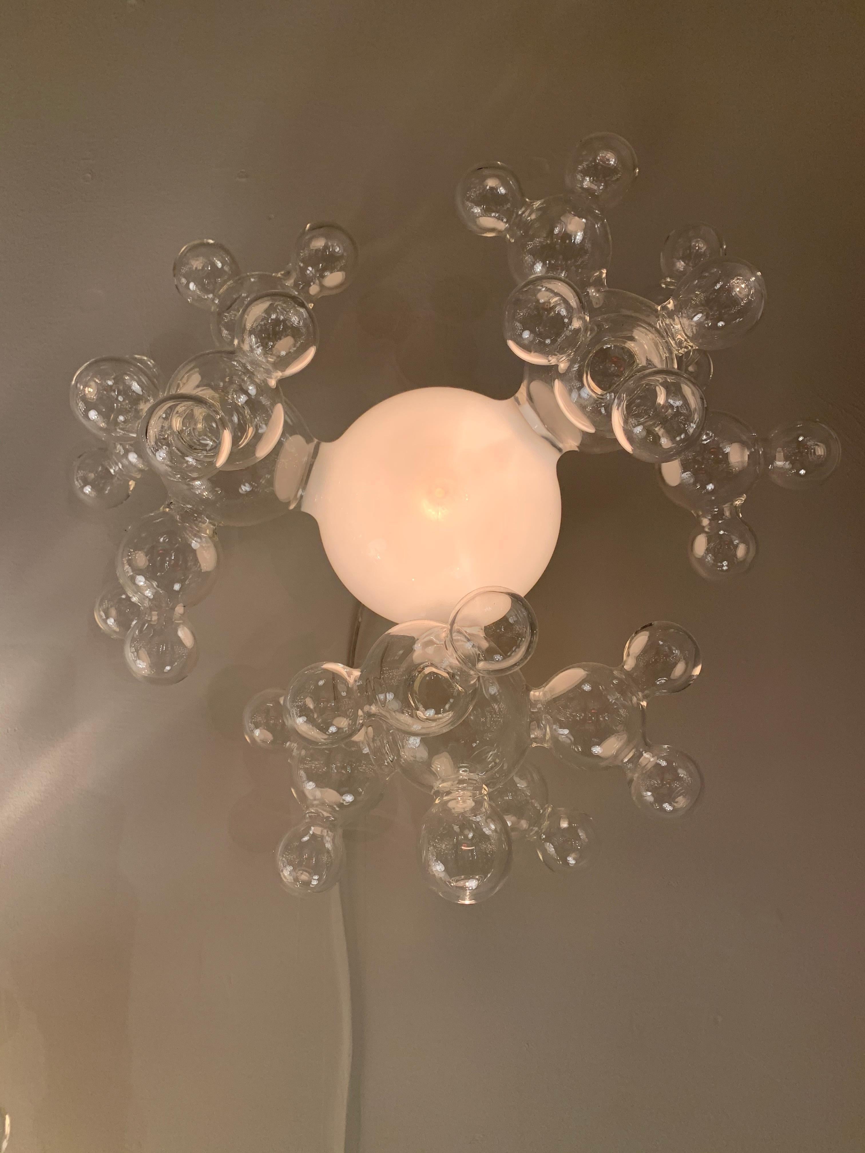 Globo in vetro bianco circondato da gruppi di bolle in vetro borosilicato chiaro, montato su una staffa in oro spazzolato. Sono disponibili dimensioni, forme e finiture personalizzate.