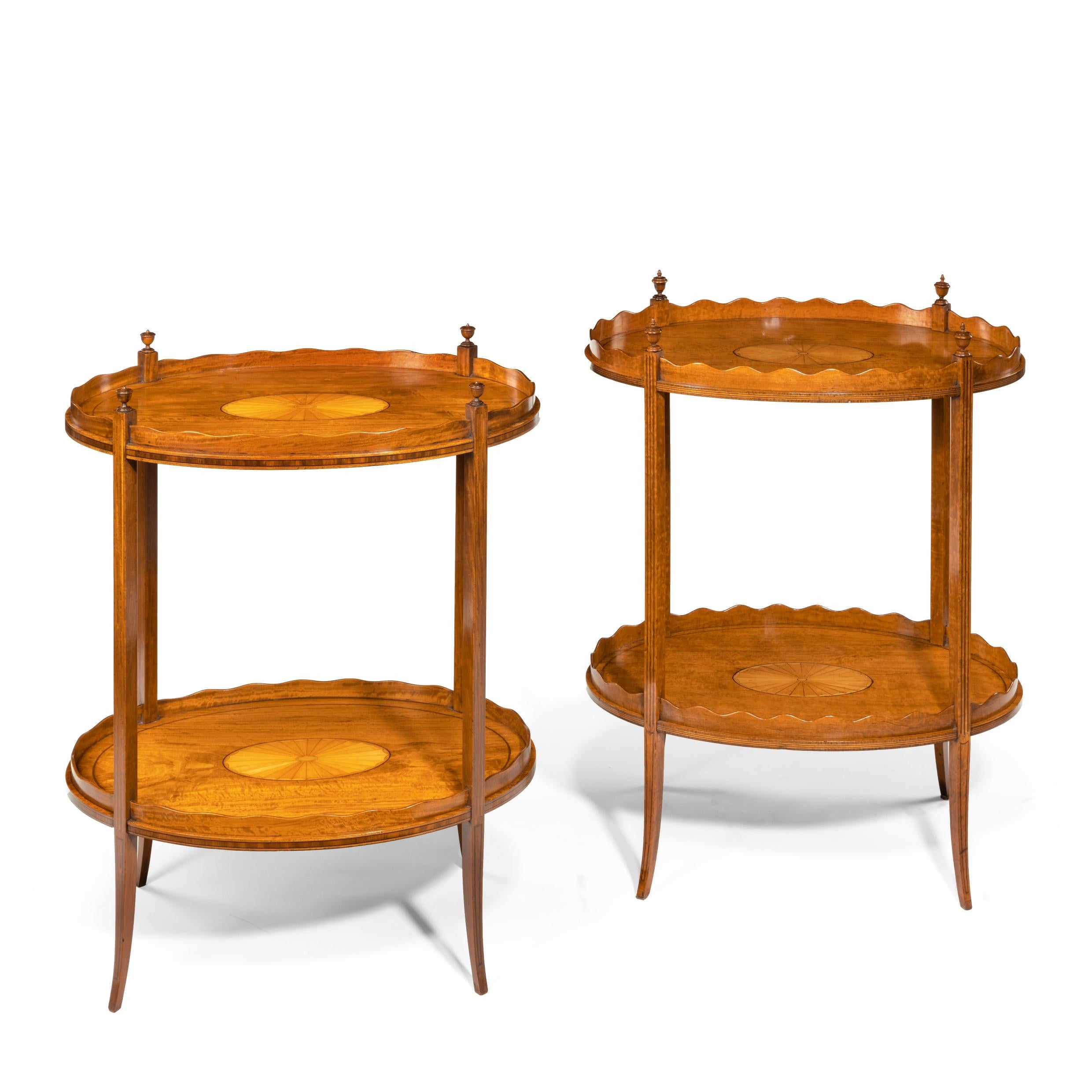 A matched pair of late Victorian satinwood tray tables, each of oval form with two tiers with solid undulating galleries, the slender square section legs surmounted by urn finials, decorated with flame veneers centered on a sunburst. English,