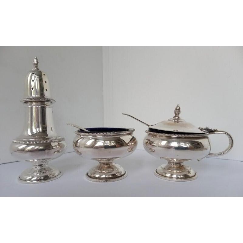 This lovely set consists of a salt dip, pepper pot, mustard pot and two spoons. The items all have cobalt blue glass inserts in excellent condition. The three items stand on circular pedestal feel and have delicate borders. Hallmarks: Made by RM &