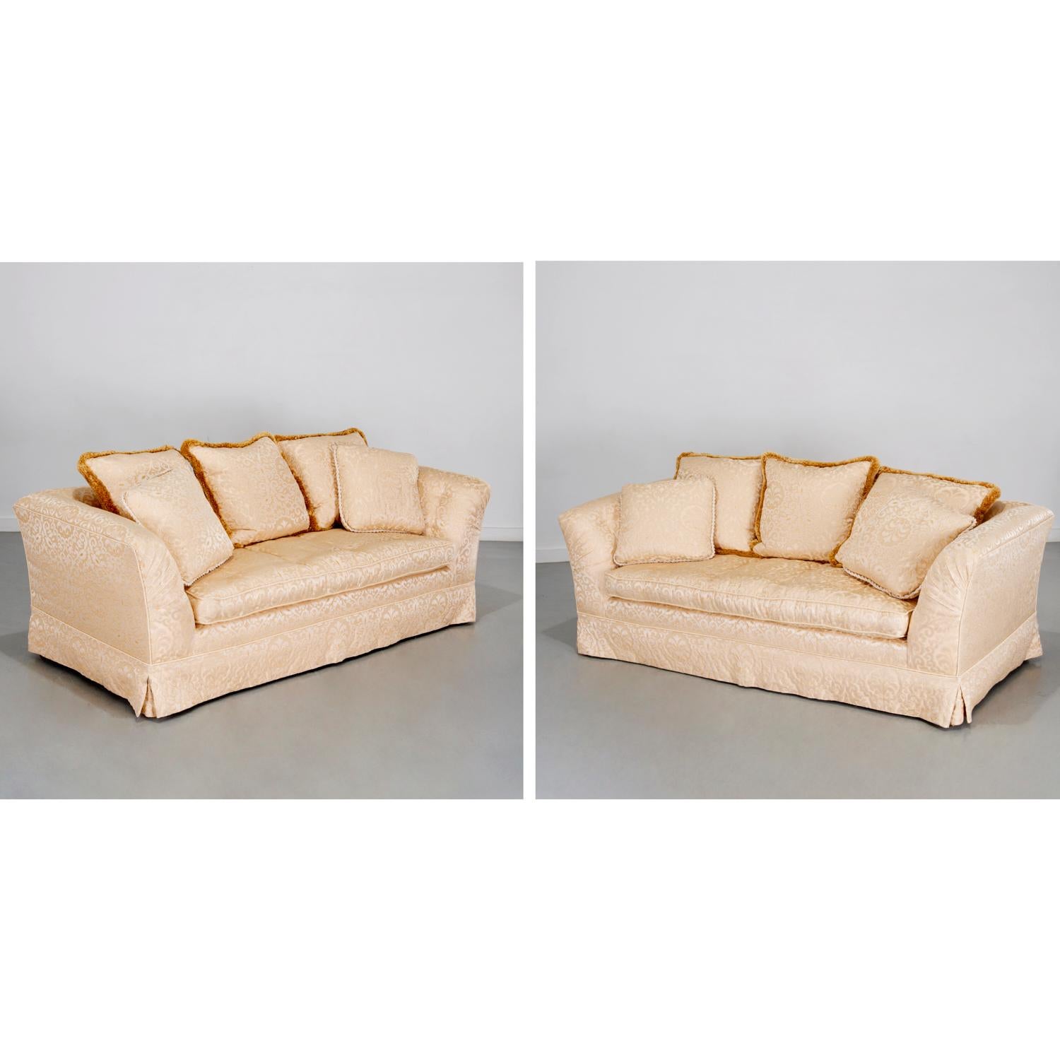 Late 20th c., USA, a pair of custom sumptuous three-seat sofas of squared form with slightly flared arms and tight back. They are upholstered in a cream and champagne silk and cotton damask with a pleated skirt over simple wood legs, unmarked. The