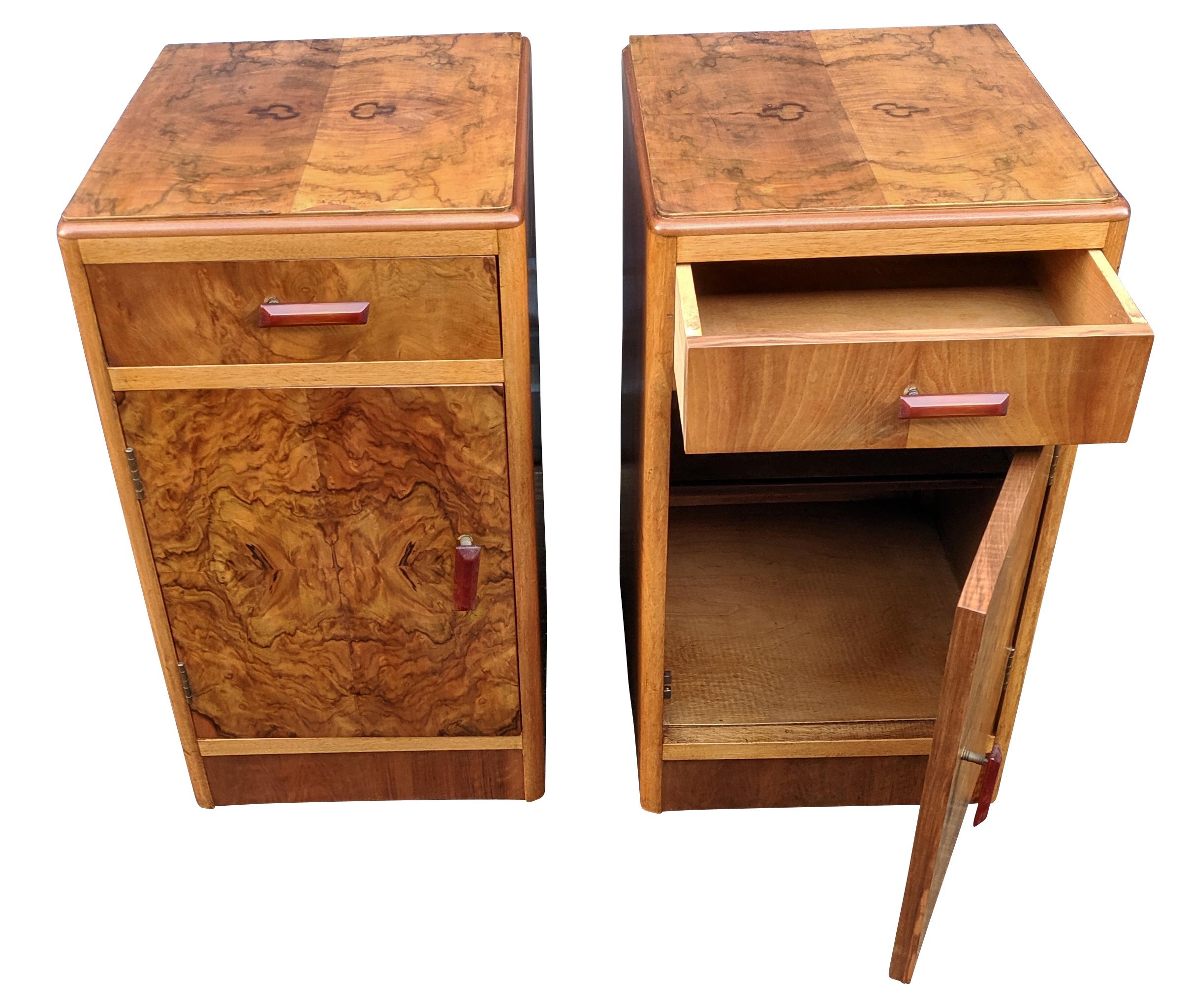 Fabulous pair of matching 1930s Art Deco bedside tables in heavily figured walnut veneer and original red bakelite phenolic handles. Two generously sized internal storage areas. Each cabinet has a pull out / pull-out upper drawer which works